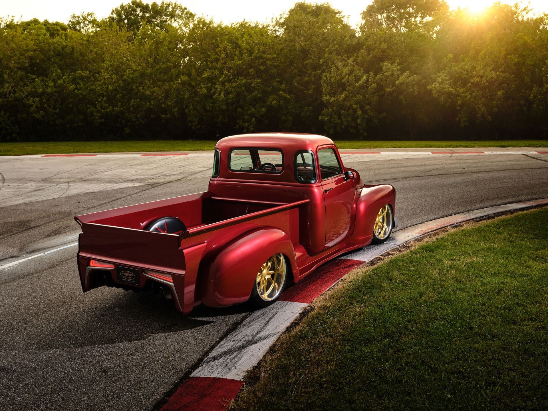Red vintage pickup truck parked on a curved road at sunset beside trees and grass