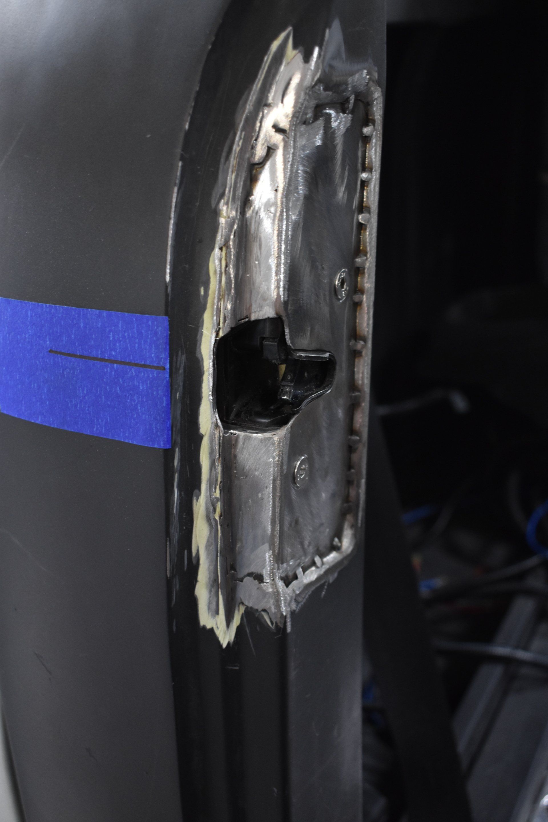 Close-up of a damaged black metal panel with a blue stripe and a broken hole in the center