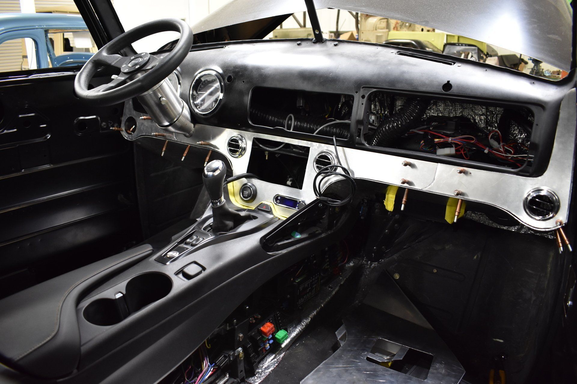 Stripped car interior with black steering wheel, bare dashboard, and center console in a workshop