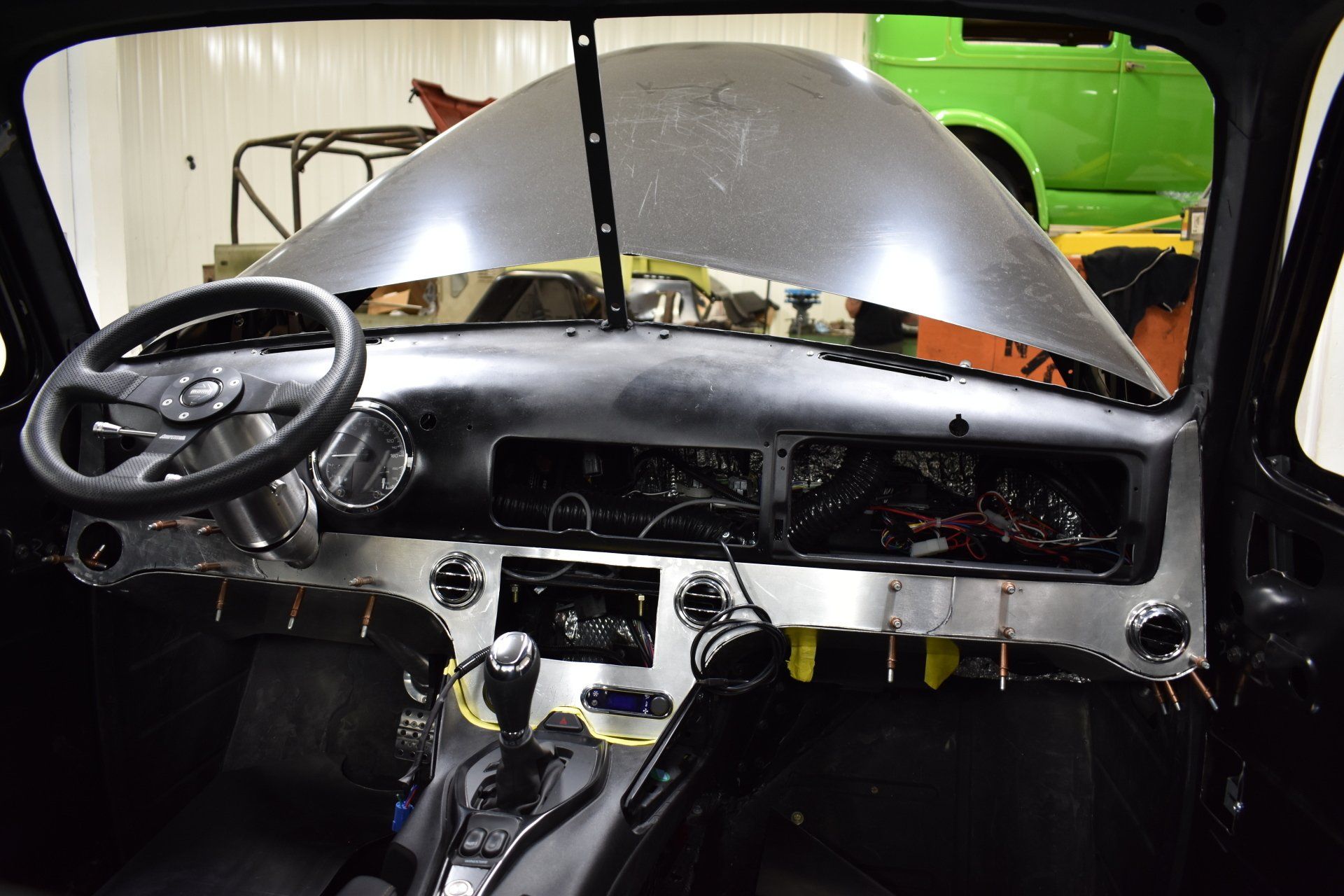 Interior of a car with a damaged windshield and exposed dashboard, viewed from the driver’s seat