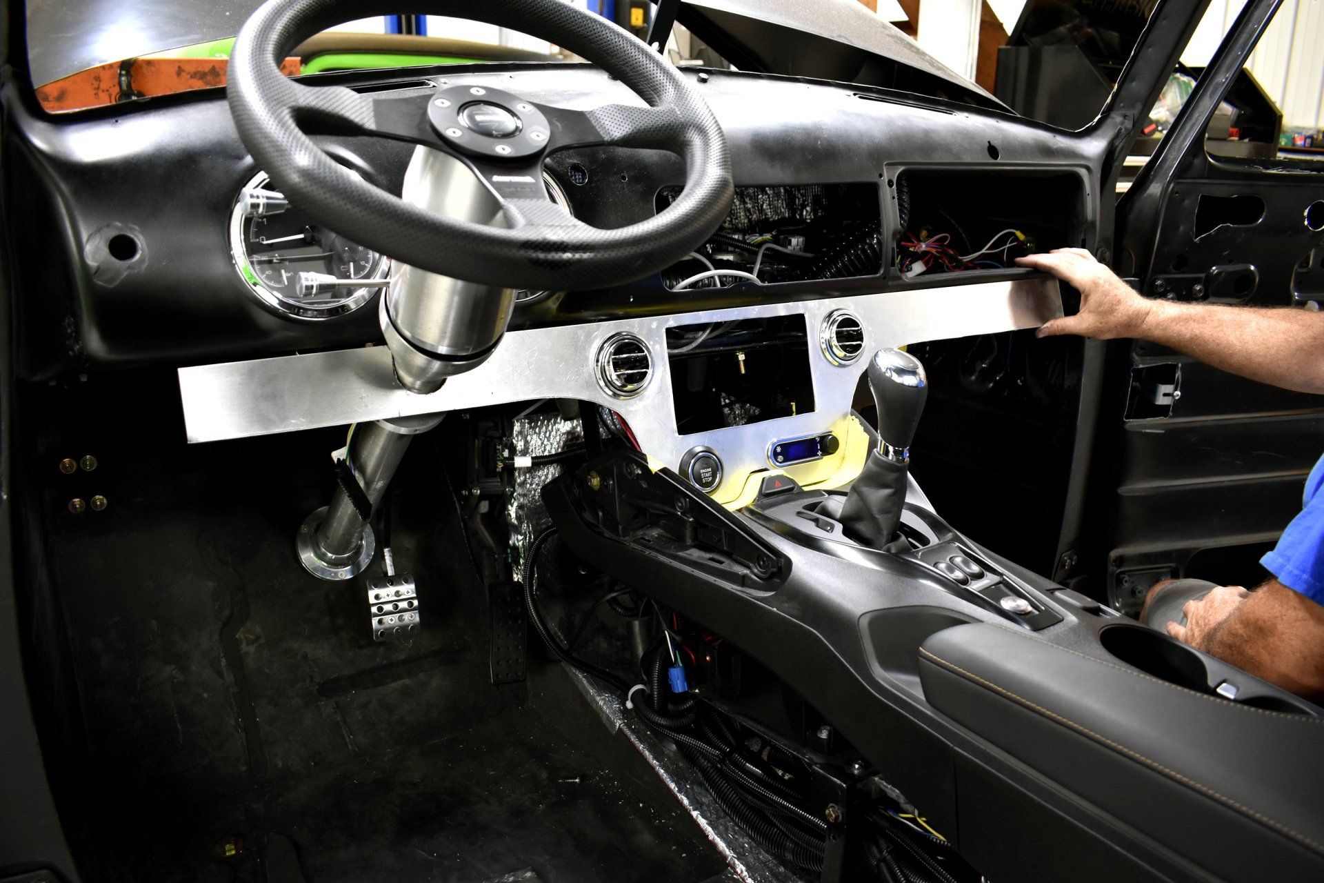 Driver’s seat interior of a car with exposed dashboard and center console, a hand reaching toward the controls