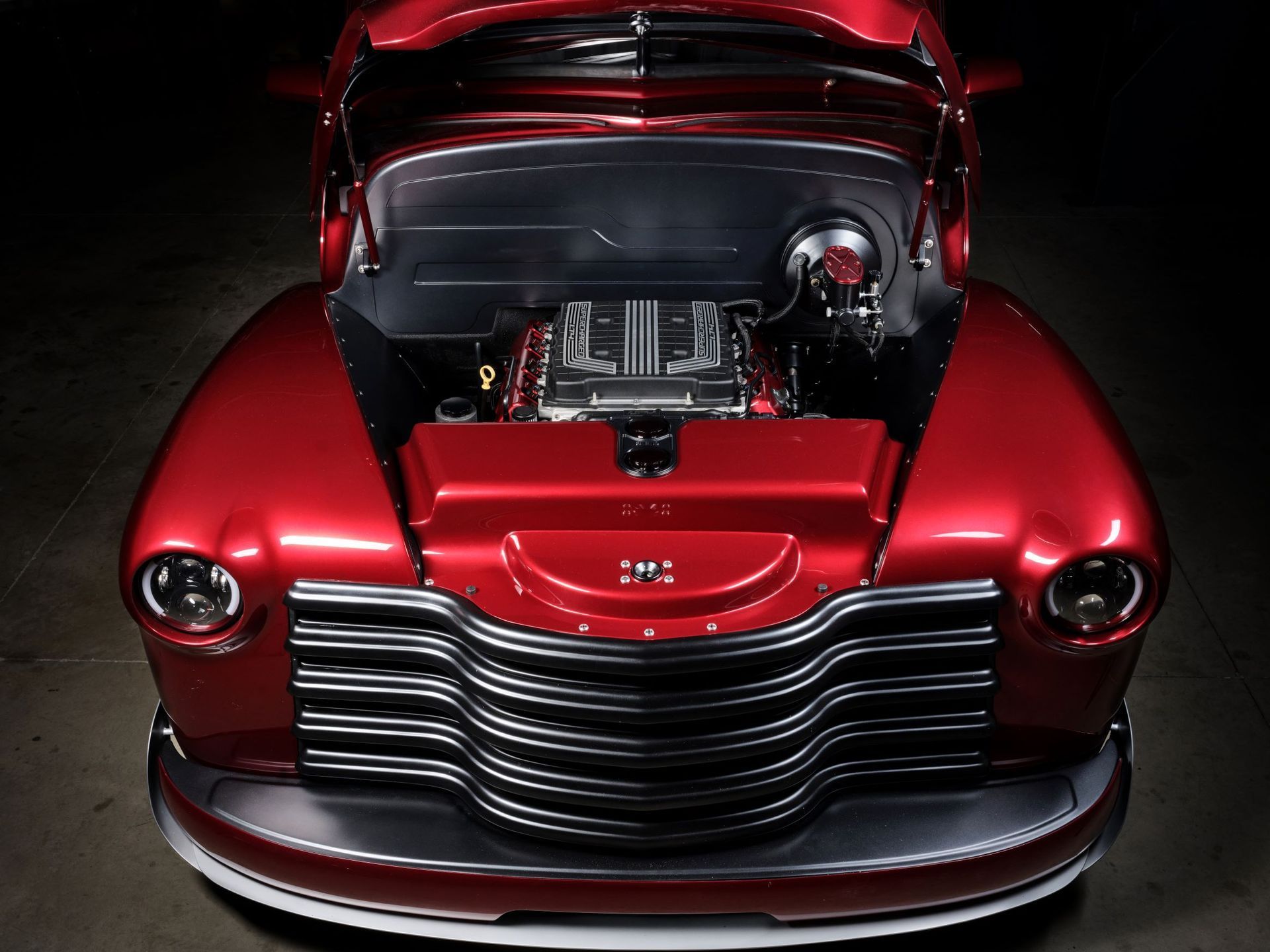 Front view of a glossy red classic car with the hood open, showing the engine on display.