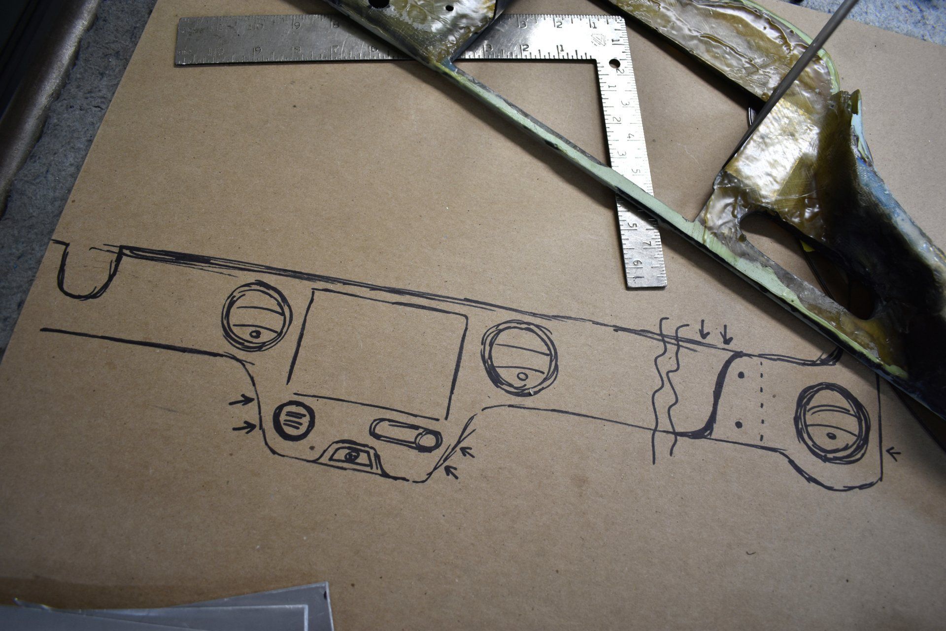 Car body panel template sketched in black on cardboard, with metal strips and tools above it