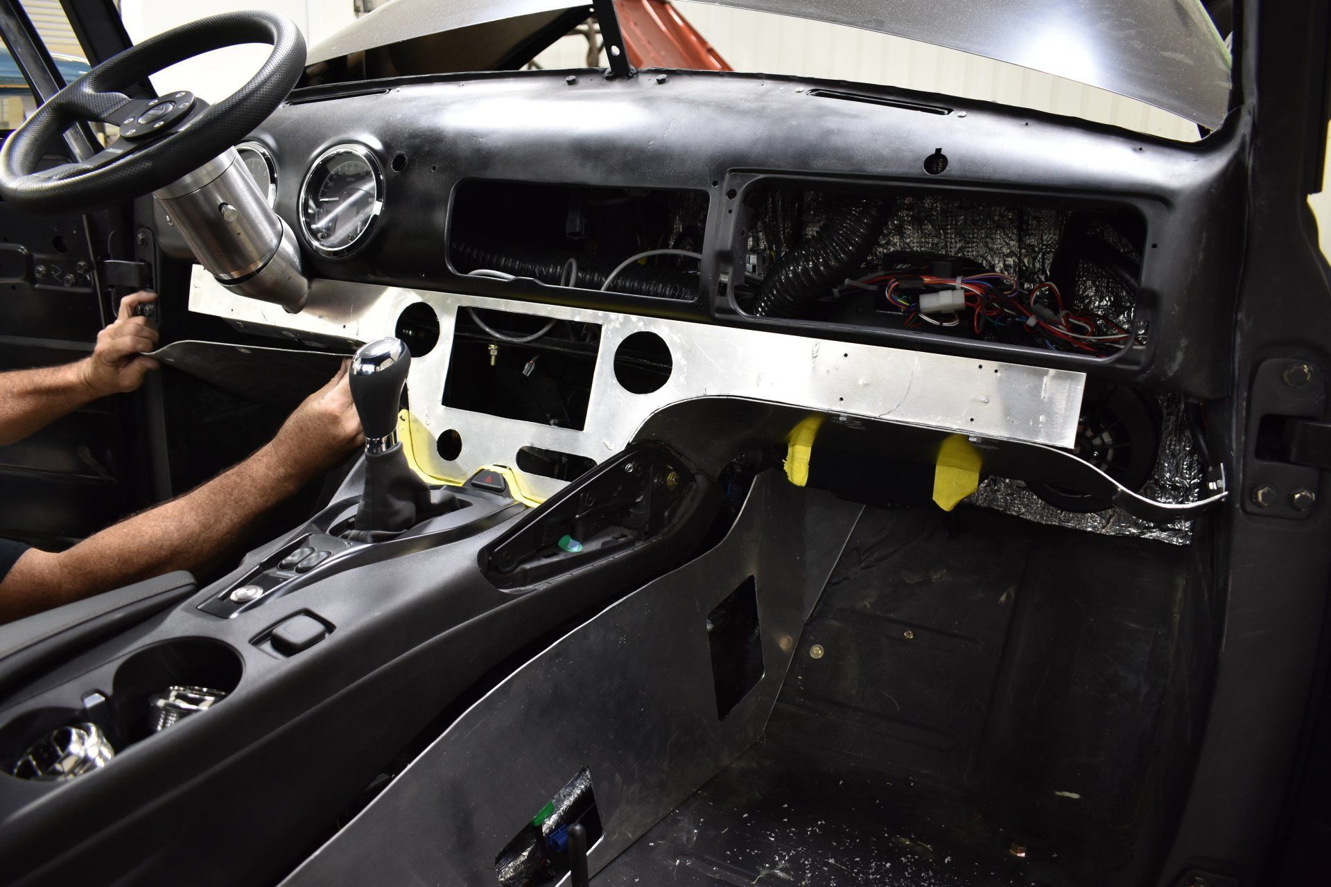 Car interior stripped to bare dashboard and wiring, with a person working on the center console area