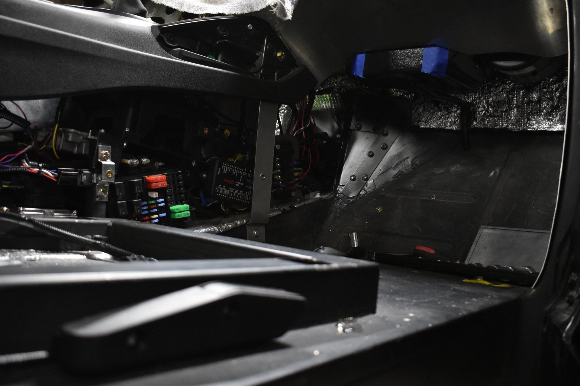 Dark interior of a car with exposed wiring, metal panels, and reflective insulation under the dashboard