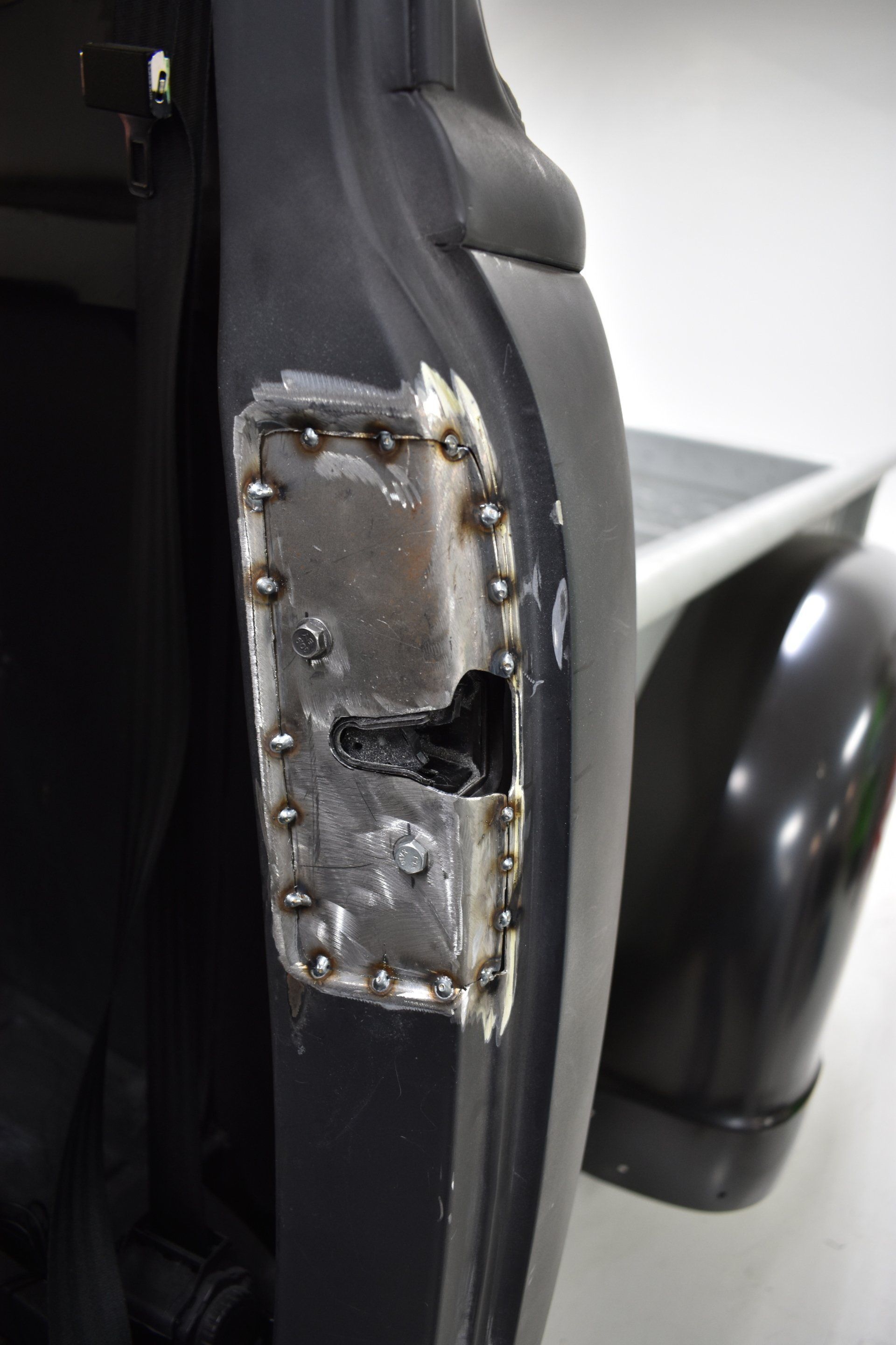 Close-up of a damaged black car door with a torn, exposed metal panel near the hinge