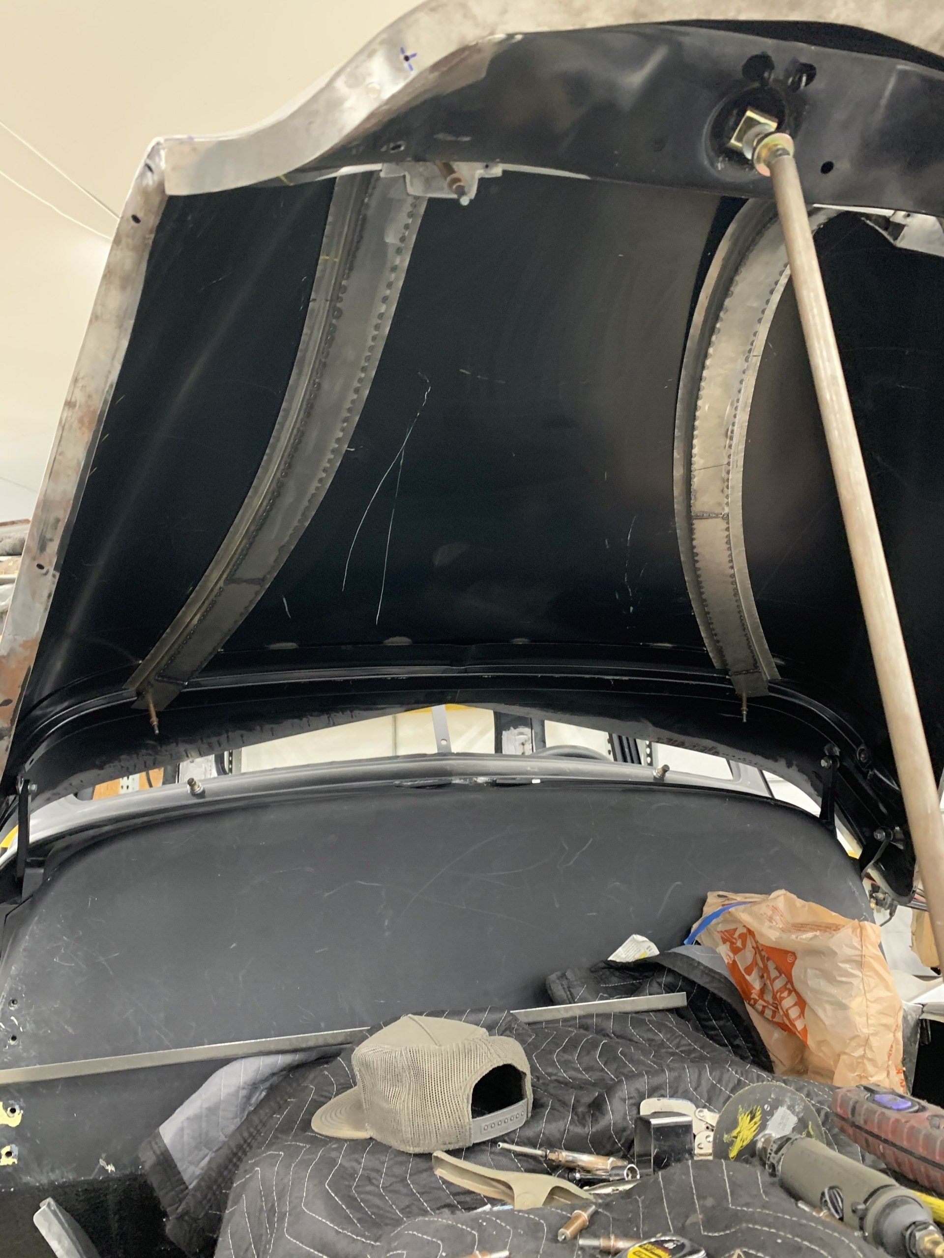 Open car hood with engine bay exposed, showing insulation, hoses, and scattered tools on the front edge