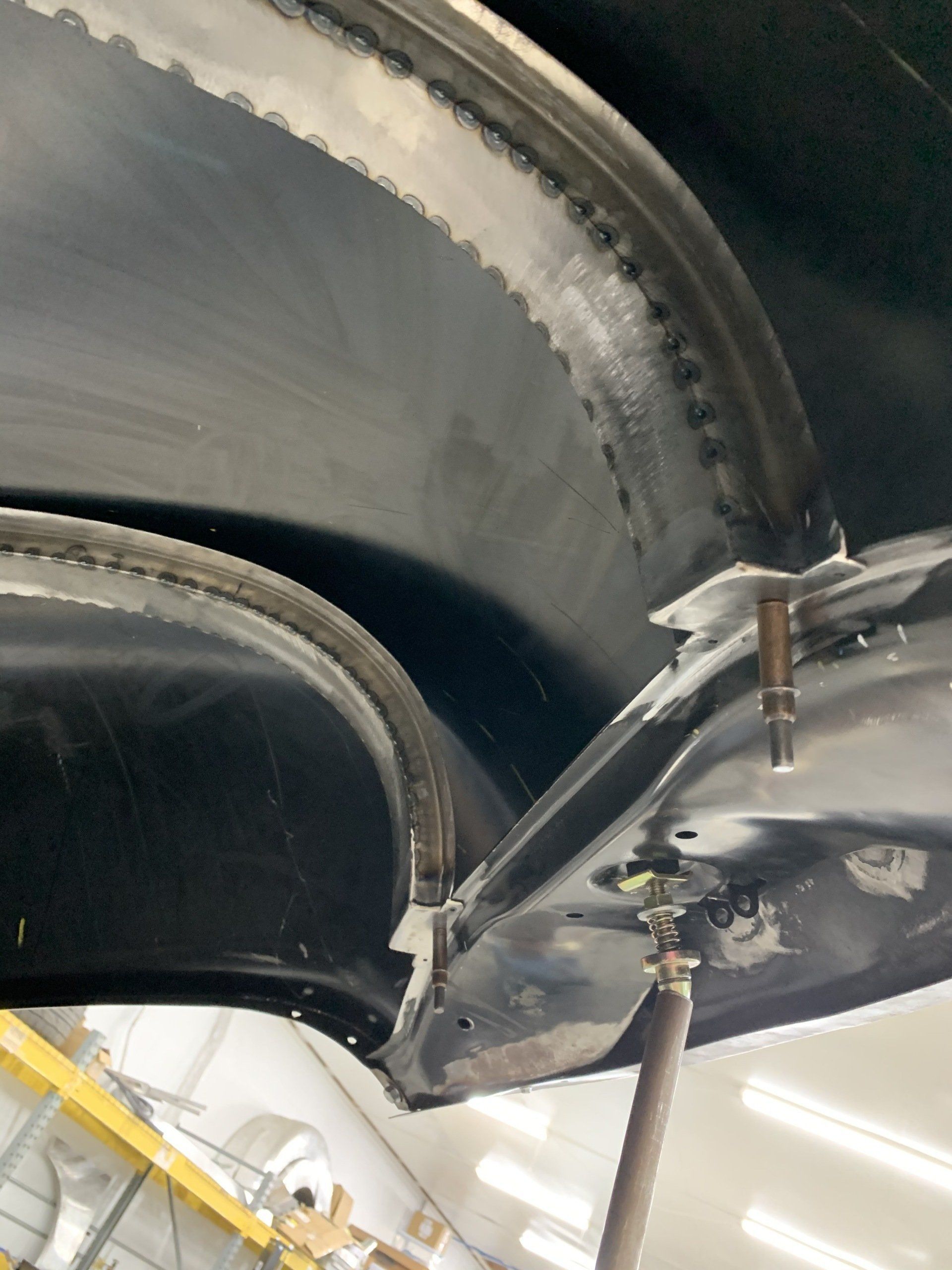 Close-up of a jet engine turbine blade assembly with metallic components and a hose in a workshop, under inspection