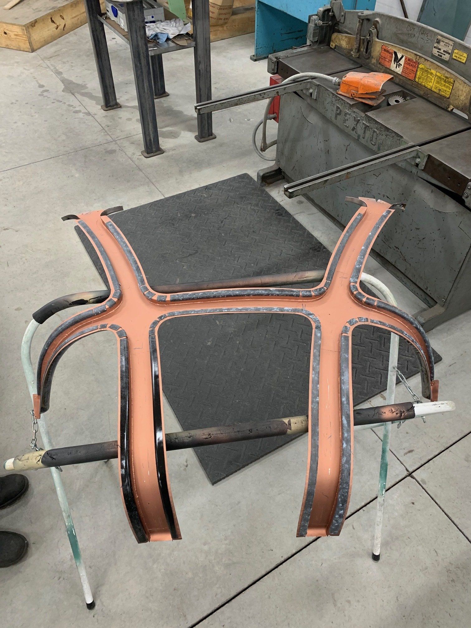 Black-and-orange upholstered chair frame on a workshop floor, resting on a metal stand.