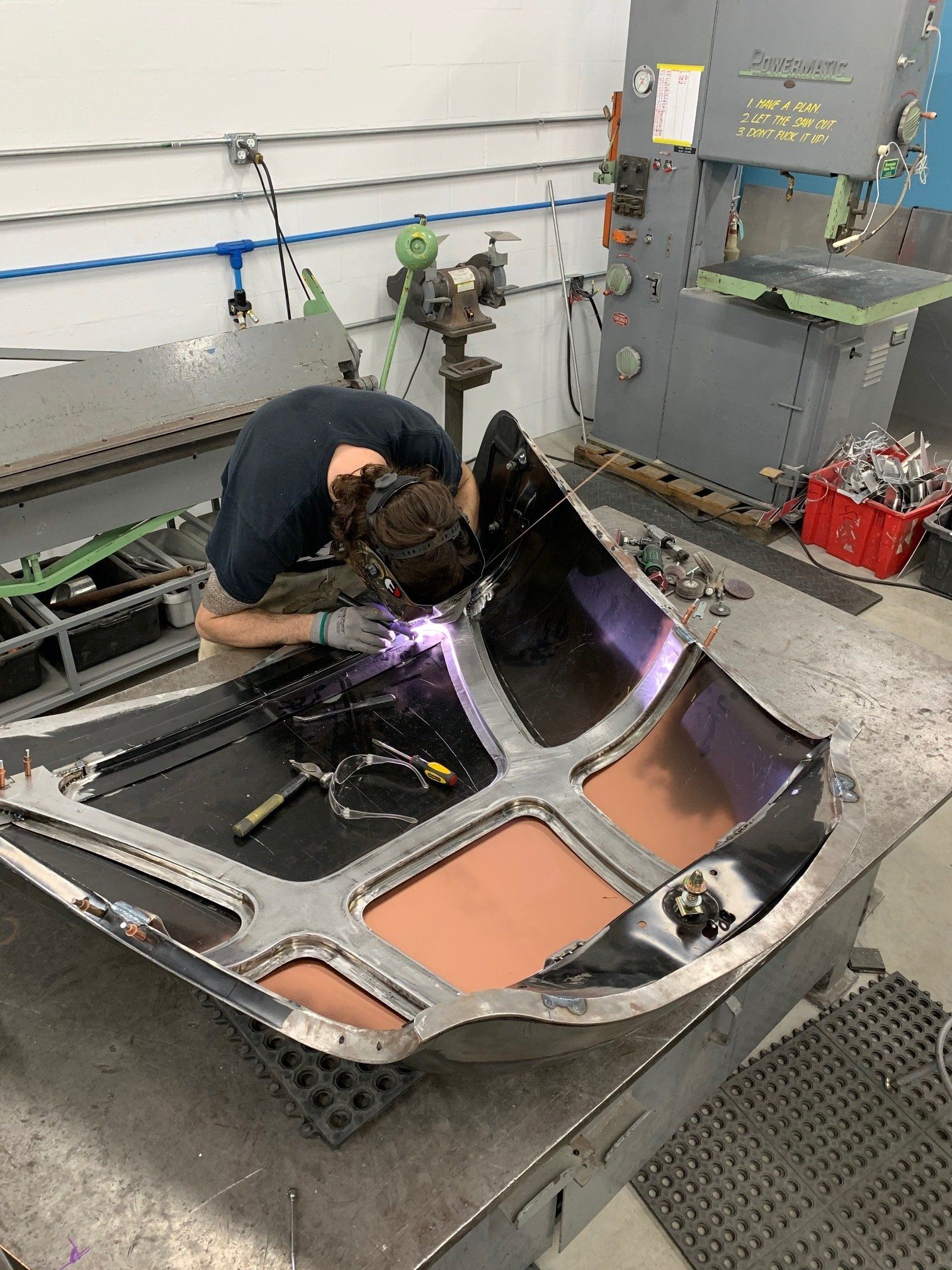Welder in a workshop repairing a metal frame, with sparks and a workbench nearby