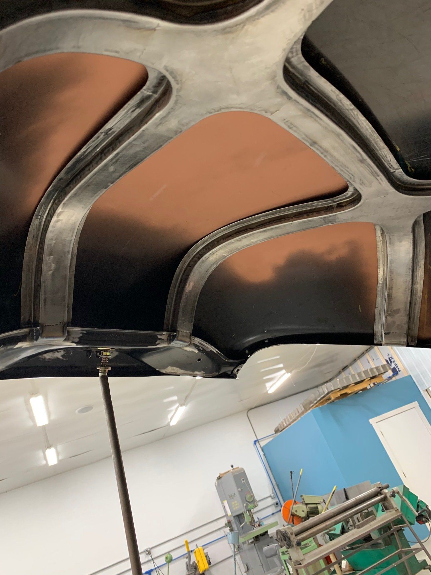 Interior of a workshop with arched ceiling panels, bright lights, and machinery near a blue wall.