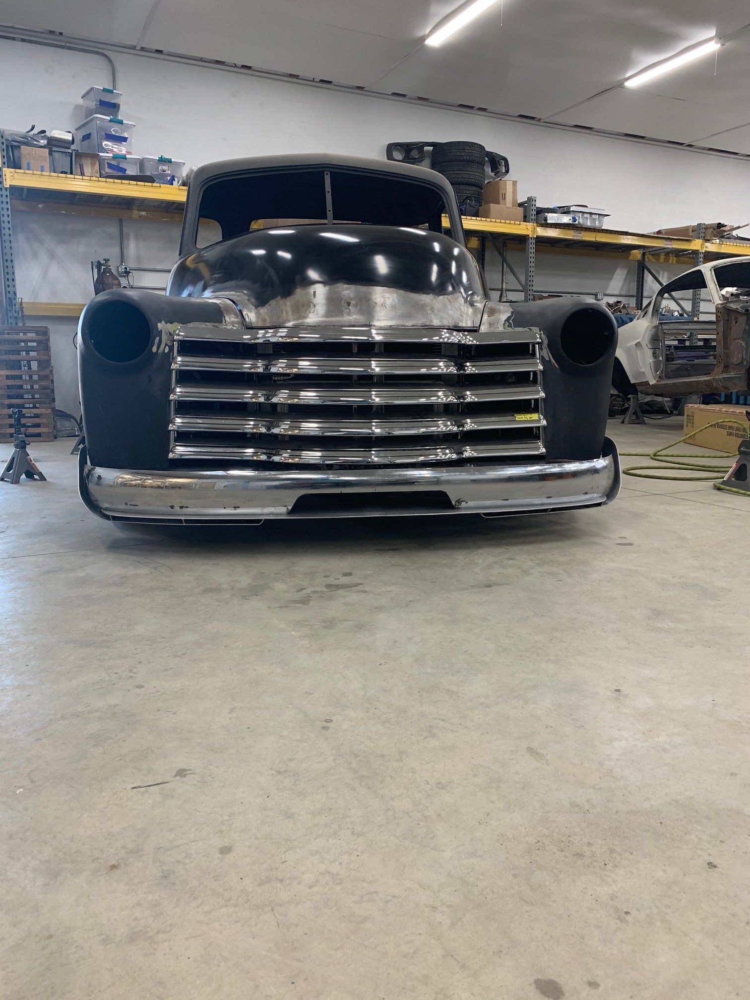 Black vintage truck front in a workshop garage, with chrome grille and round headlights.