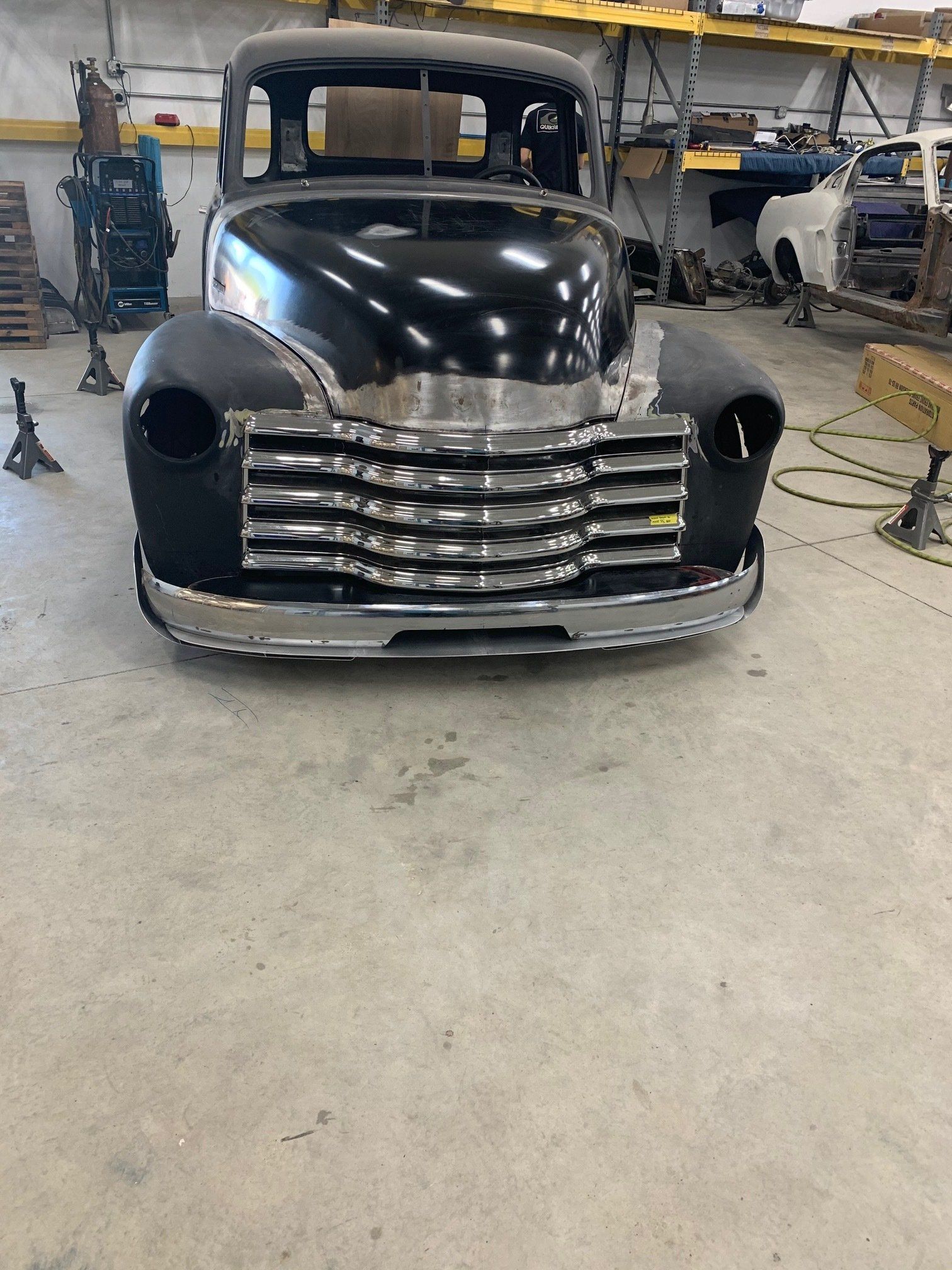Black vintage pickup truck front in a garage, with chrome grille and unfinished bodywork.