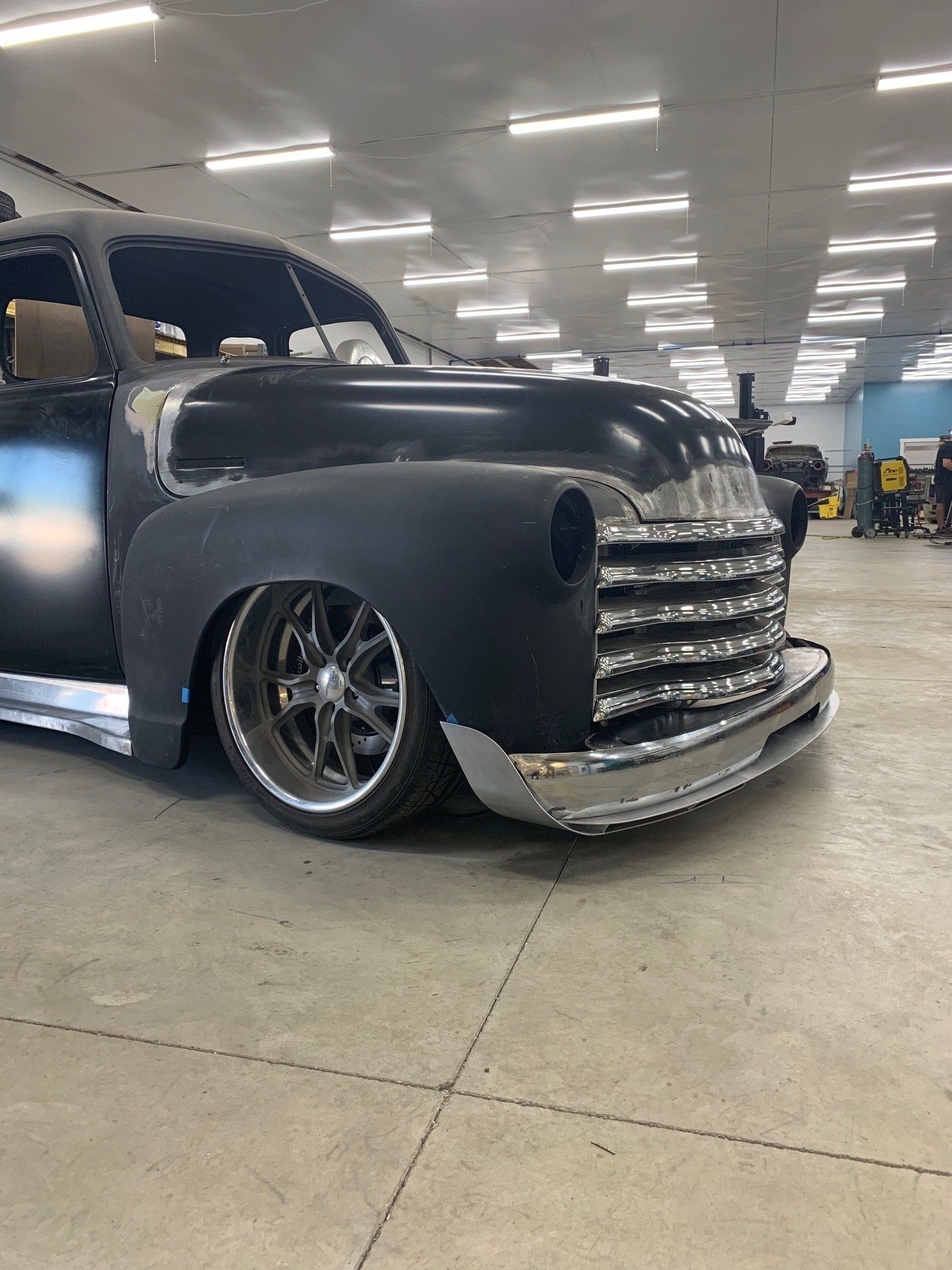 Custom black vintage pickup truck with chrome grille lowered in an indoor car show garage
