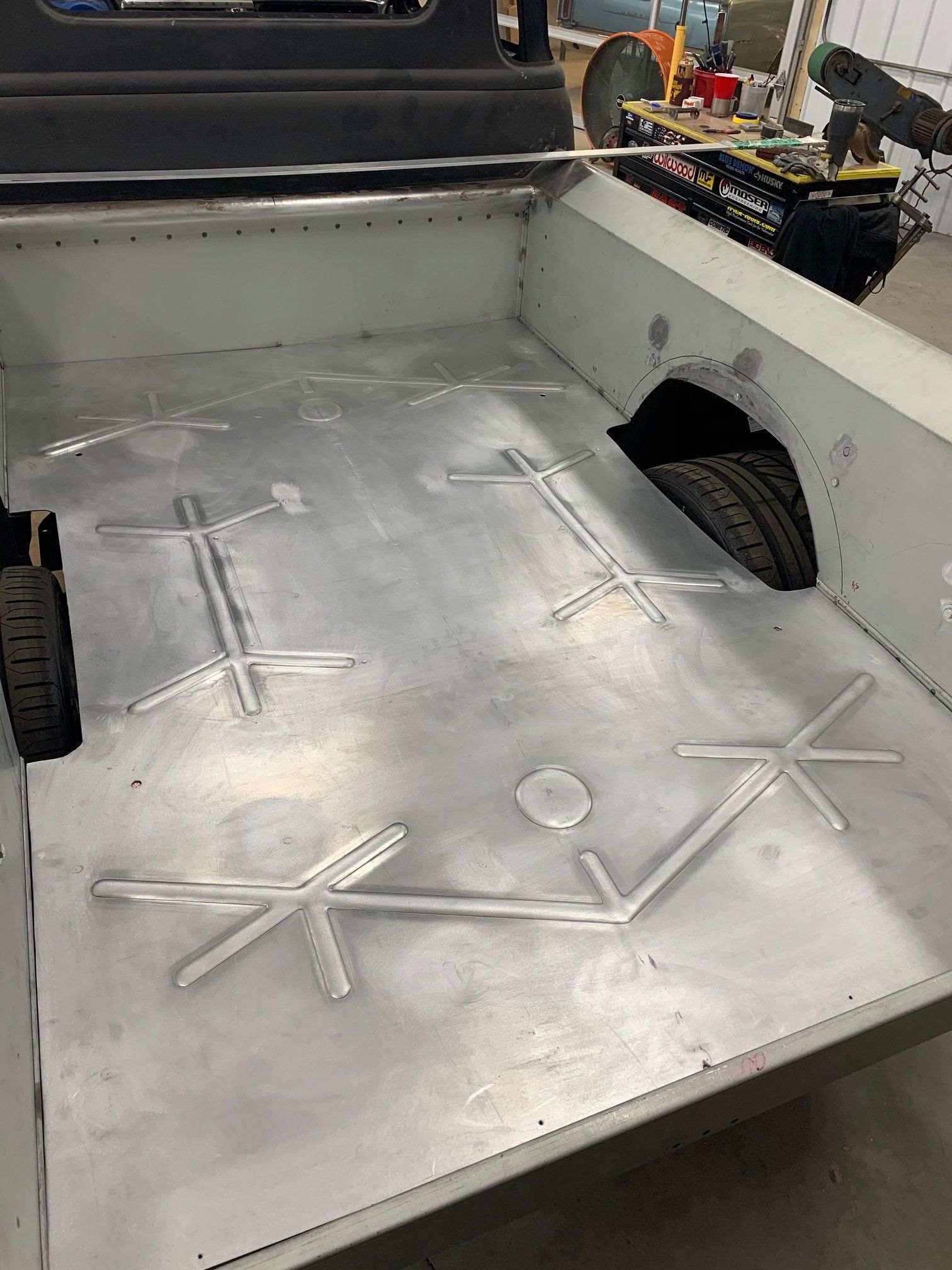 Metal truck bed liner with white tie-down anchors and side wheel well cutouts.