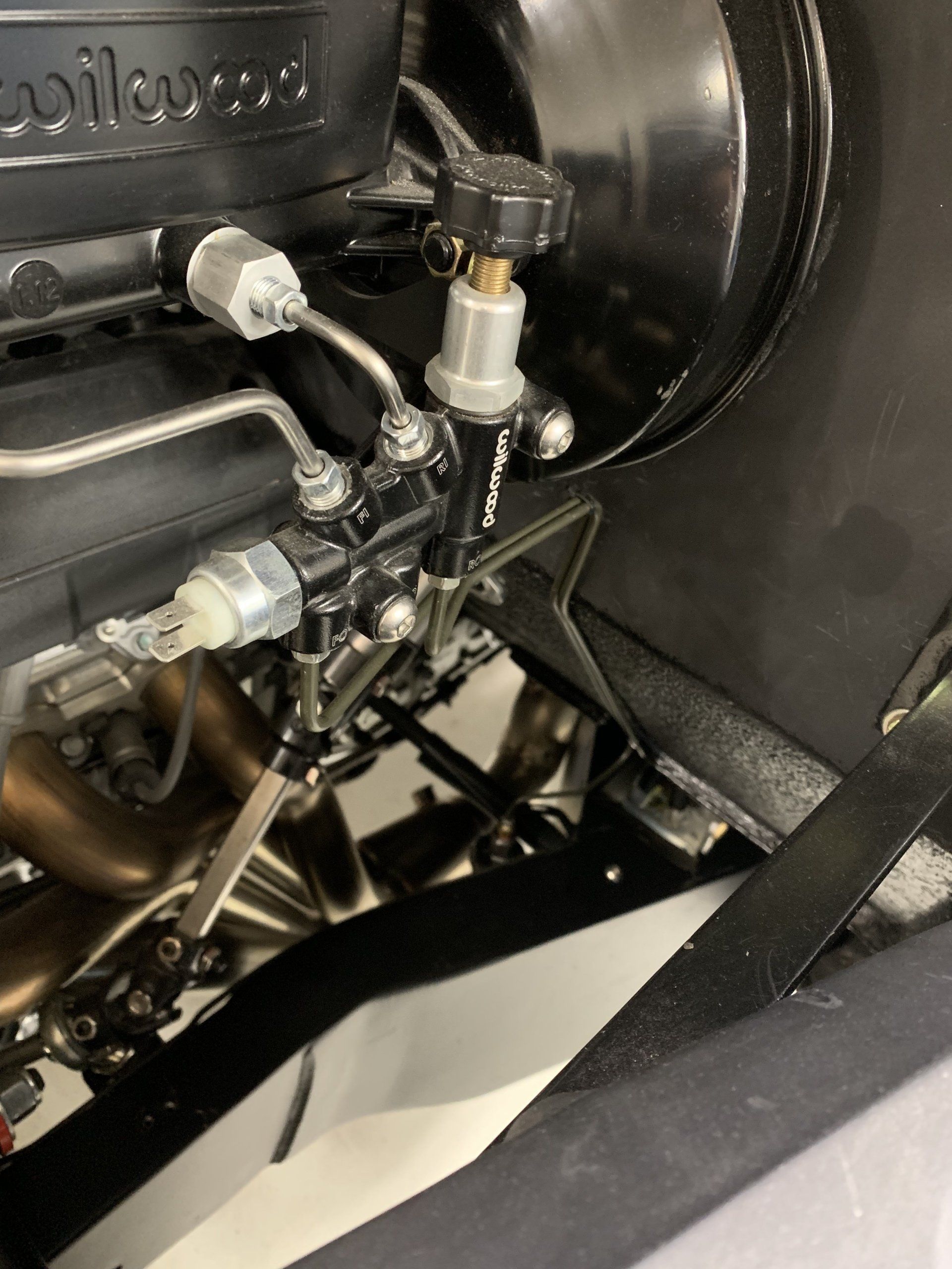 Close-up of a black mechanical component with metal fittings, hoses, and a white connector inside a machine