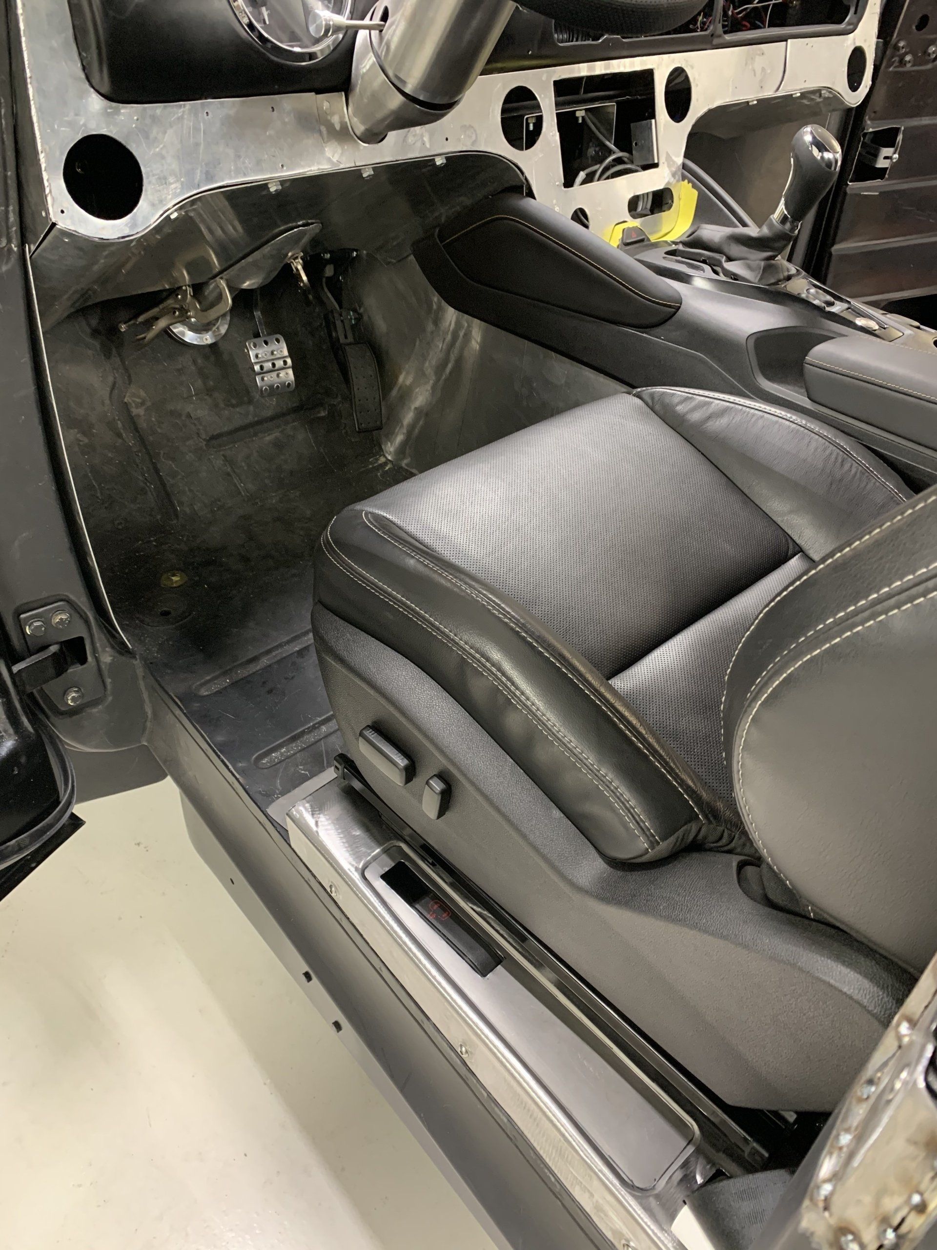 Car interior with removed dashboard, showing black leather front seat and exposed wiring on the passenger side