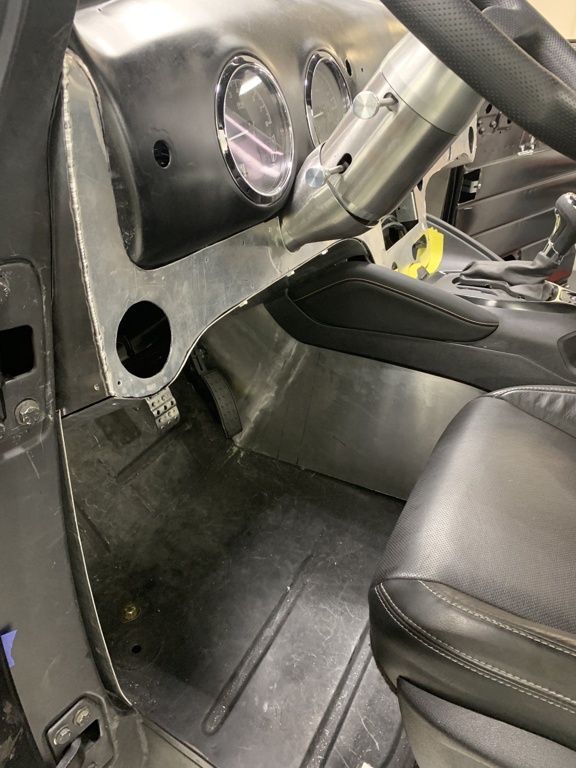 Modified car interior with black racing seats, roll cage bars, and exposed metal dashboard area