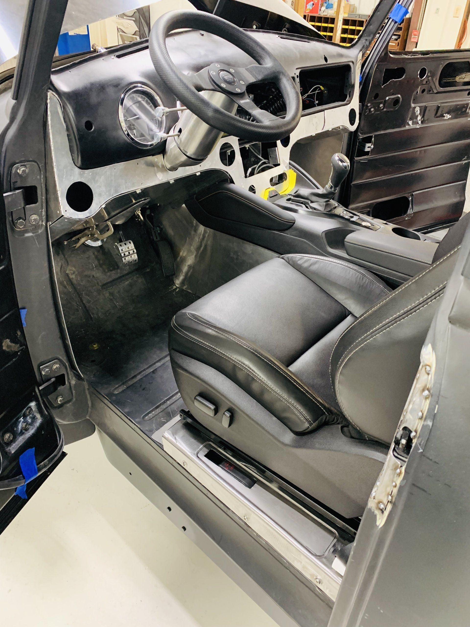 Interior of a car under restoration, showing black seats, steering wheel, and unfinished dashboard.