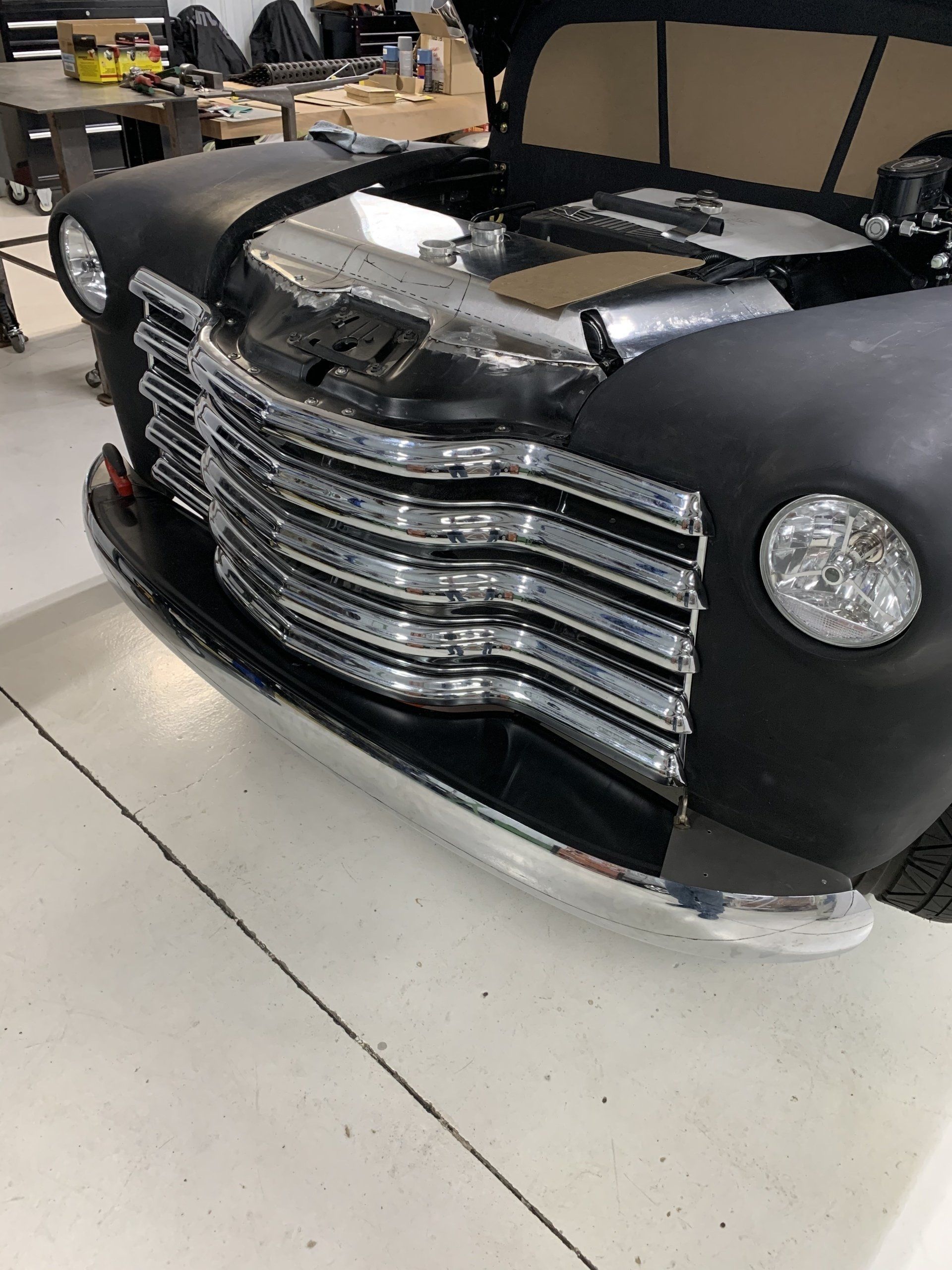 Close-up of a black classic truck front with chrome grille, shown indoors on a showroom floor