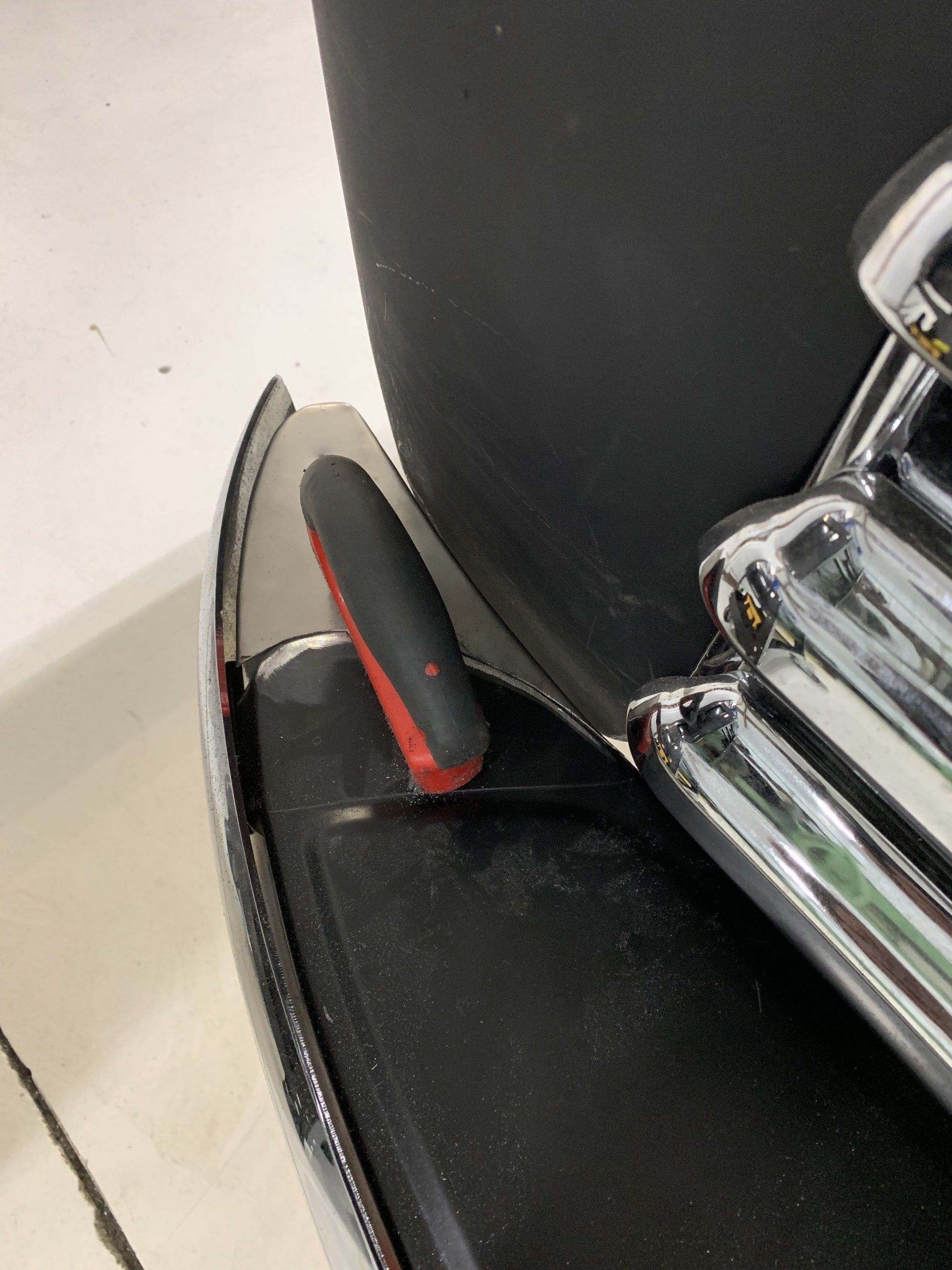 Black chair armrest with a red-handled tool or lever beside chrome wheelchair-like bars