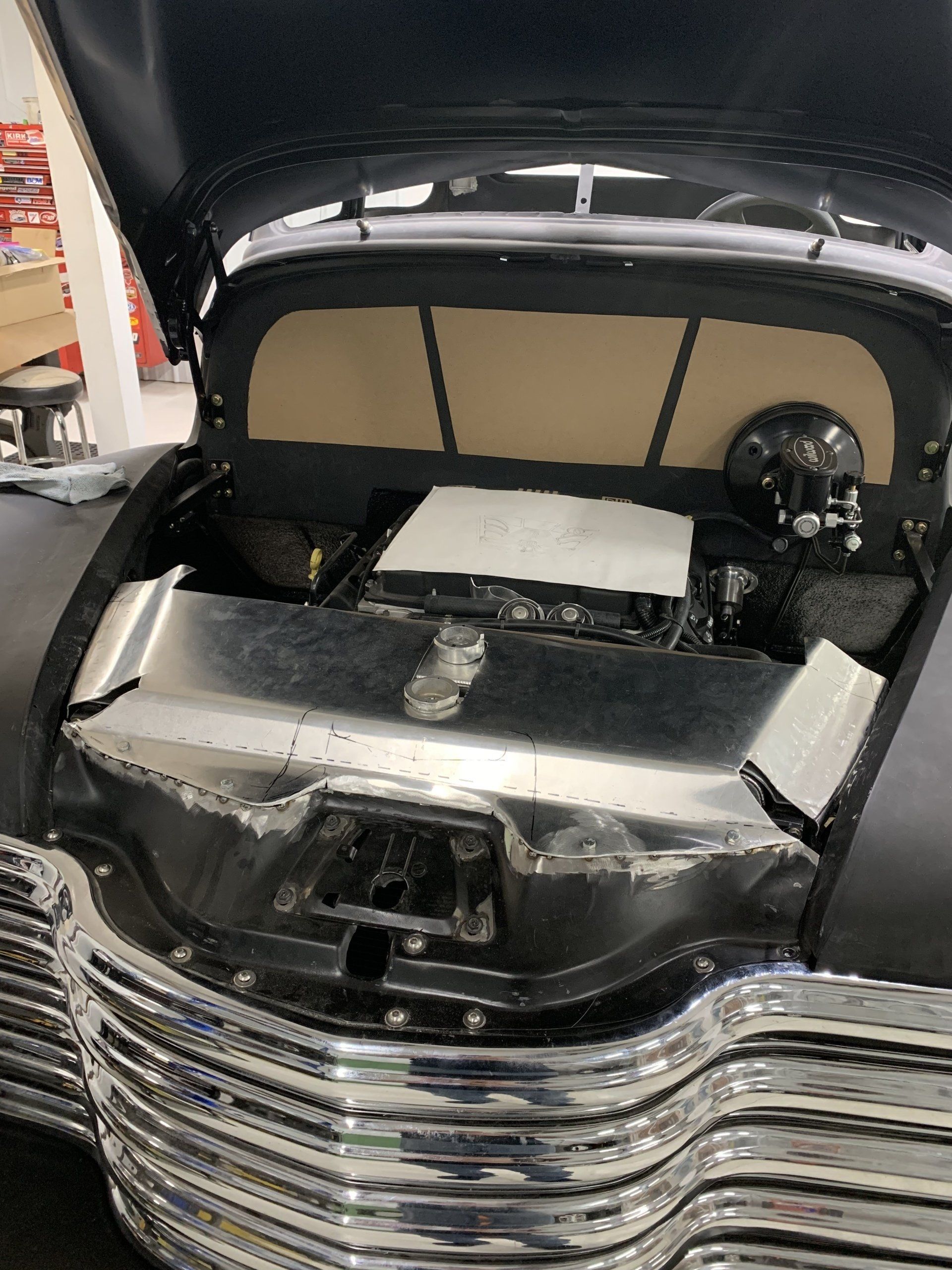 Black classic car with hood open, showing front engine compartment and chrome grille in a garage