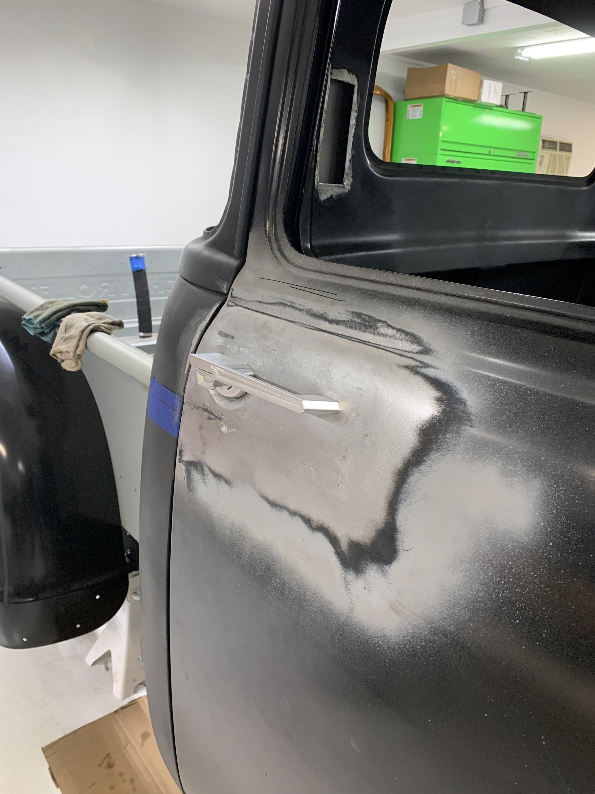 Weathered black truck cab panel with sanded body filler and primer repair near the rear window