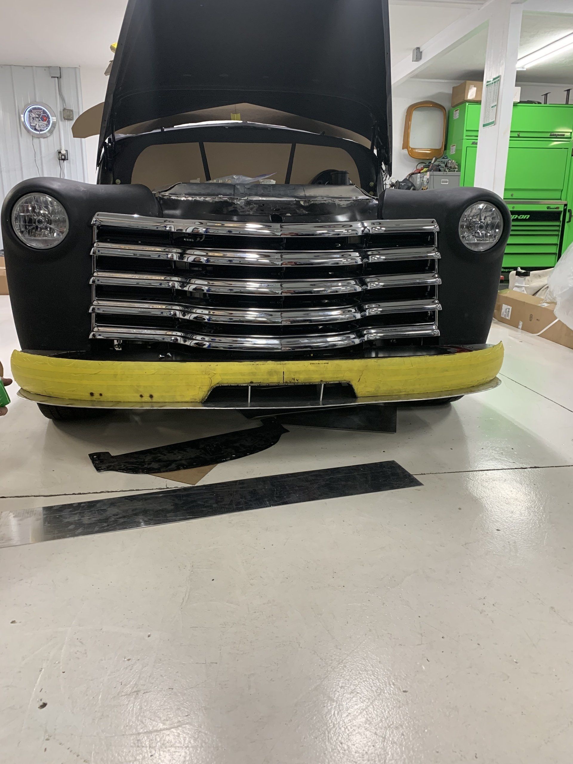 Front view of a black vintage truck with yellow bumper in a workshop garage