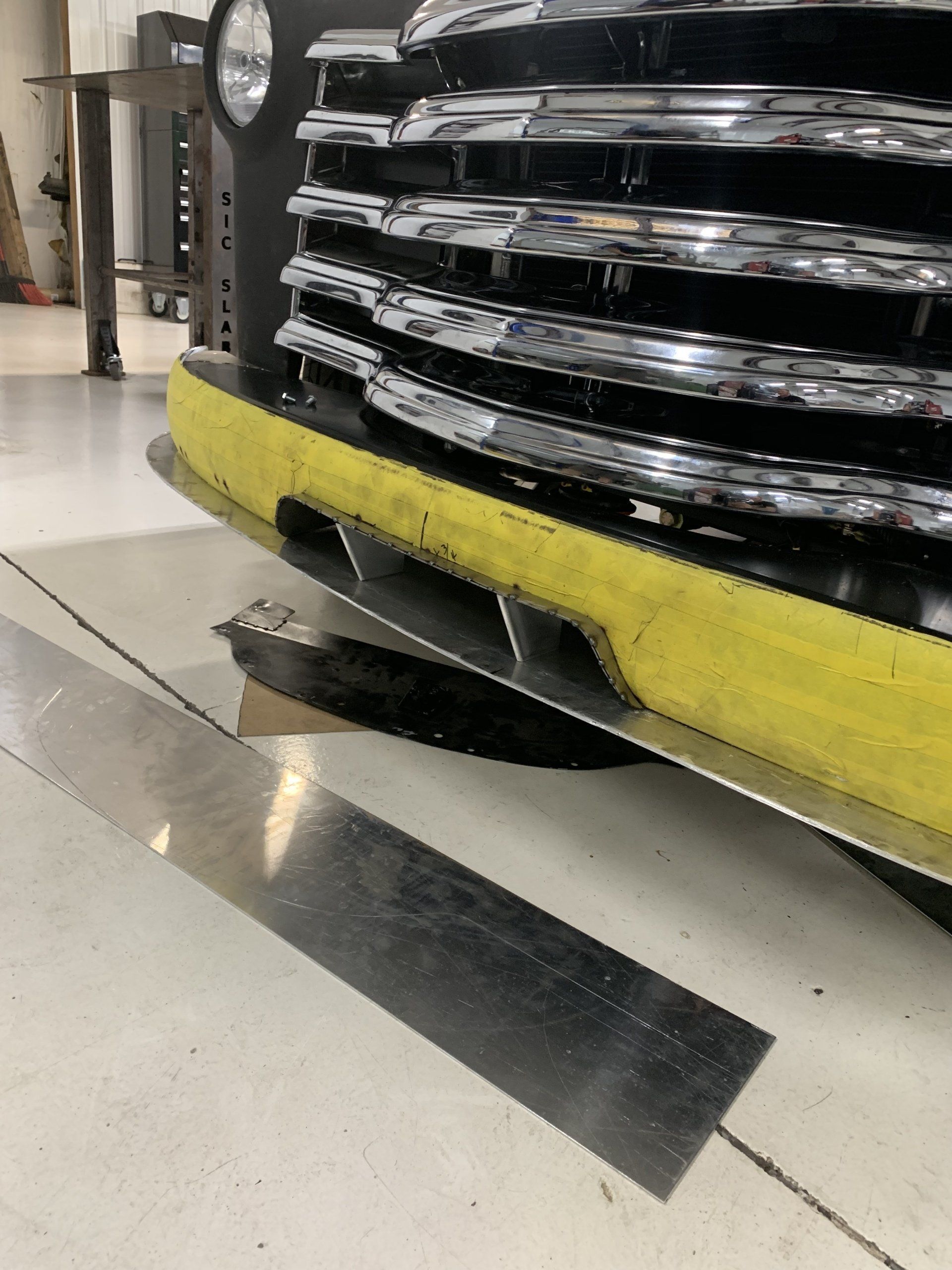 Damaged black car bumper with a yellow strip hanging over a showroom floor tile.