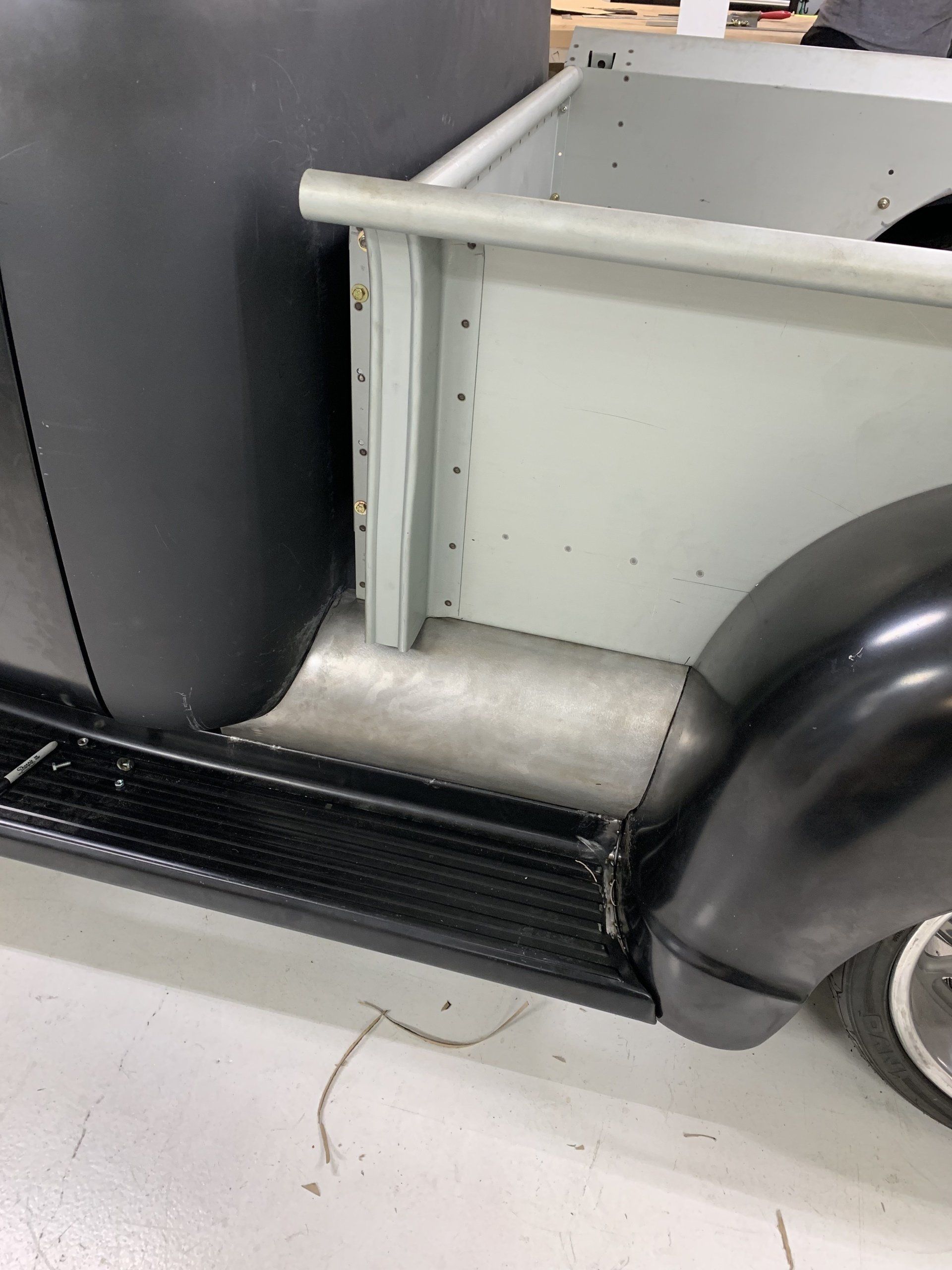 Close-up of a vintage car’s side step, rear wheel, and fender in a garage.