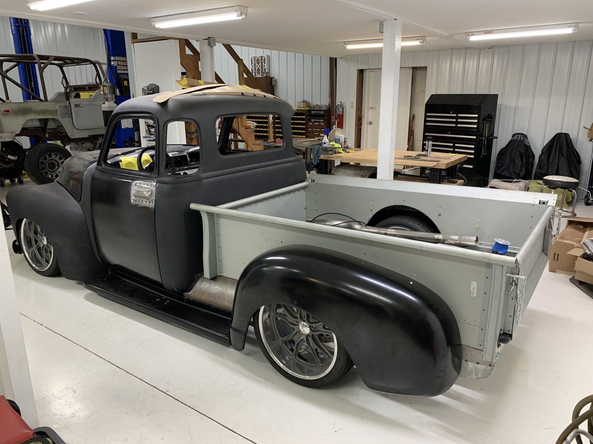 Vintage black and gray pickup truck in a workshop, viewed from the side.