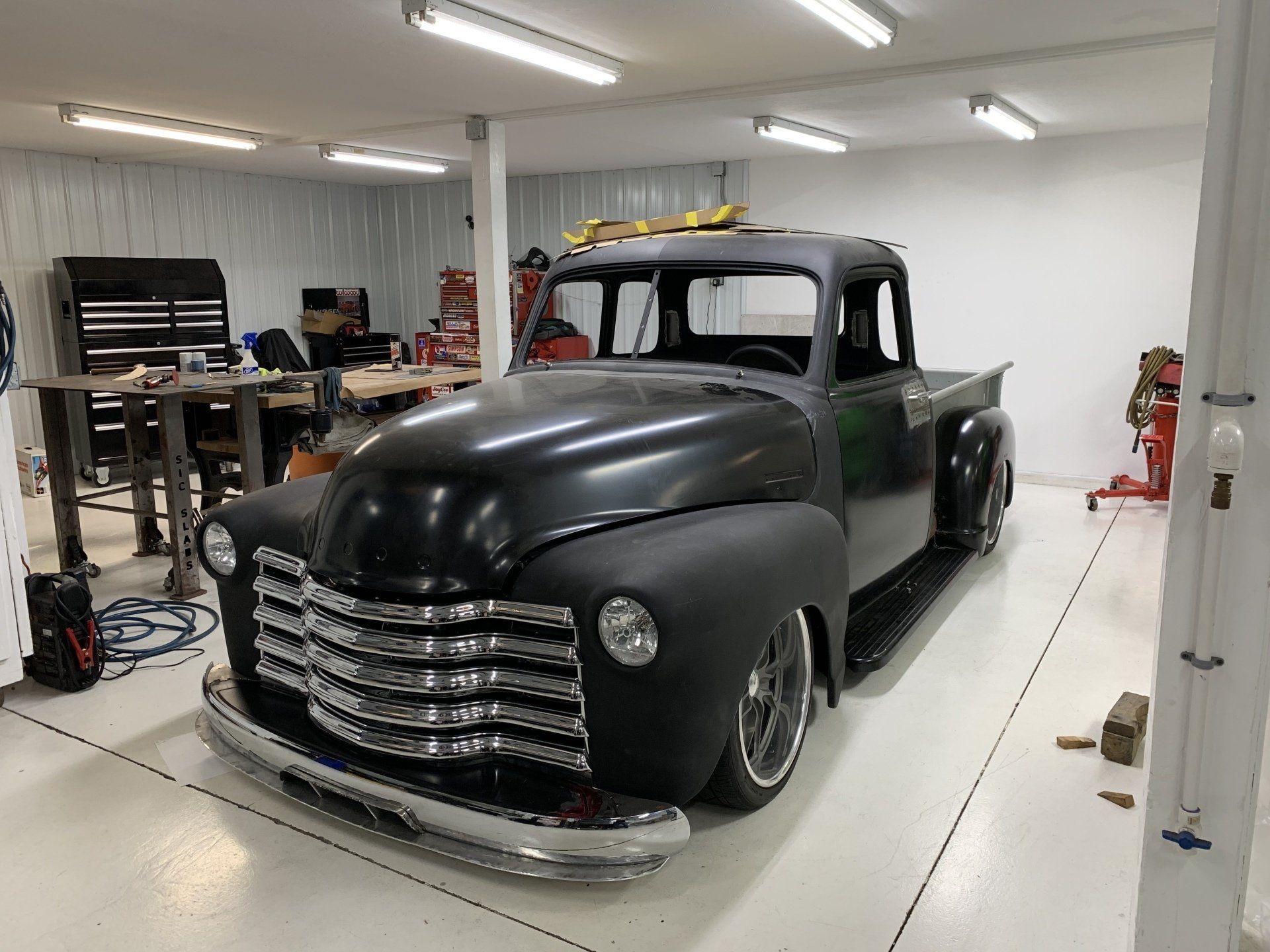 Black vintage pickup truck in a bright garage workshop with tools and equipment nearby