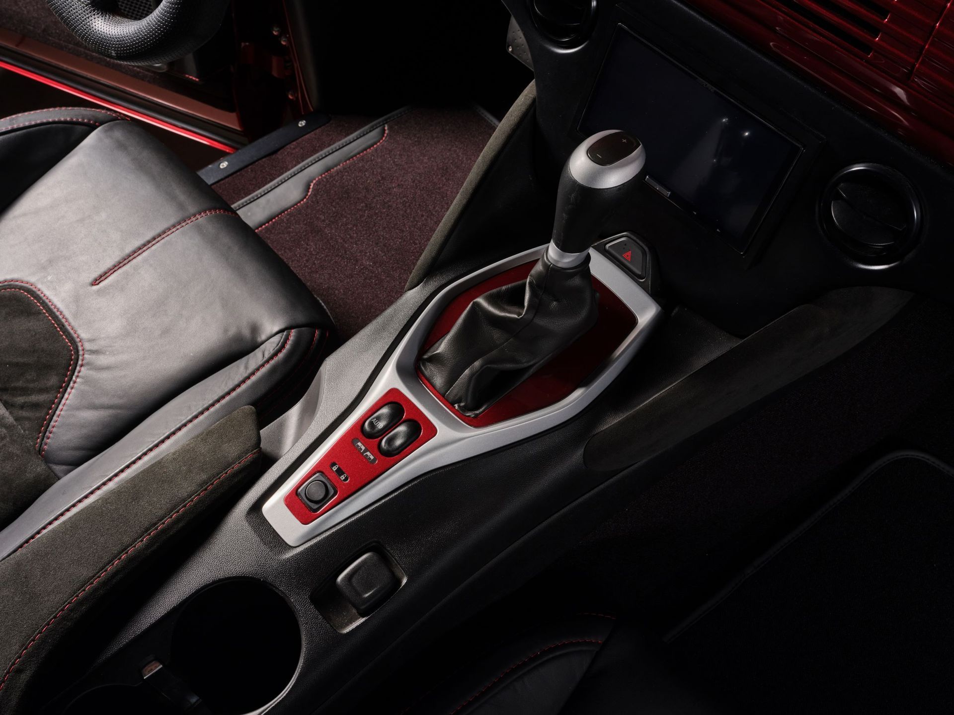 Car interior with a manual gear shift and red-trimmed center console controls.
