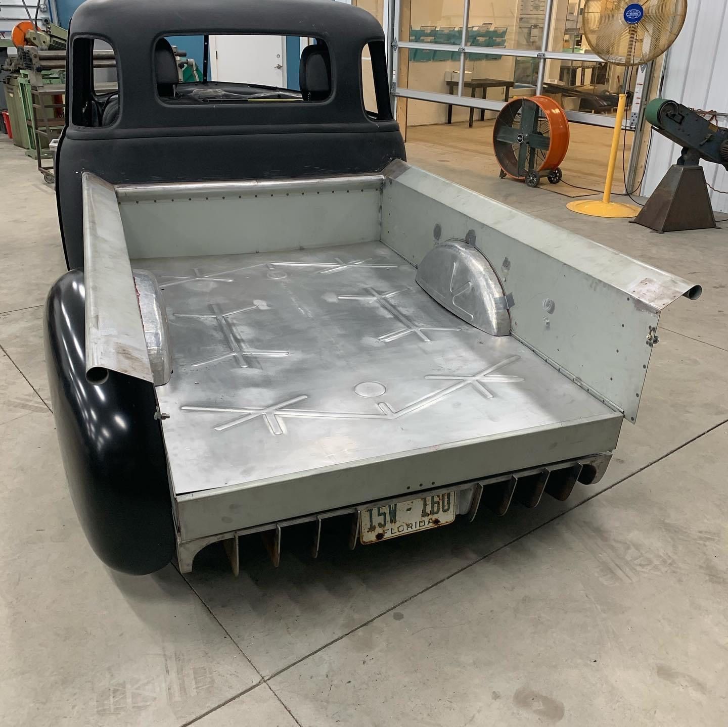 Vintage black pickup truck with a bare silver cargo bed in a workshop or museum setting