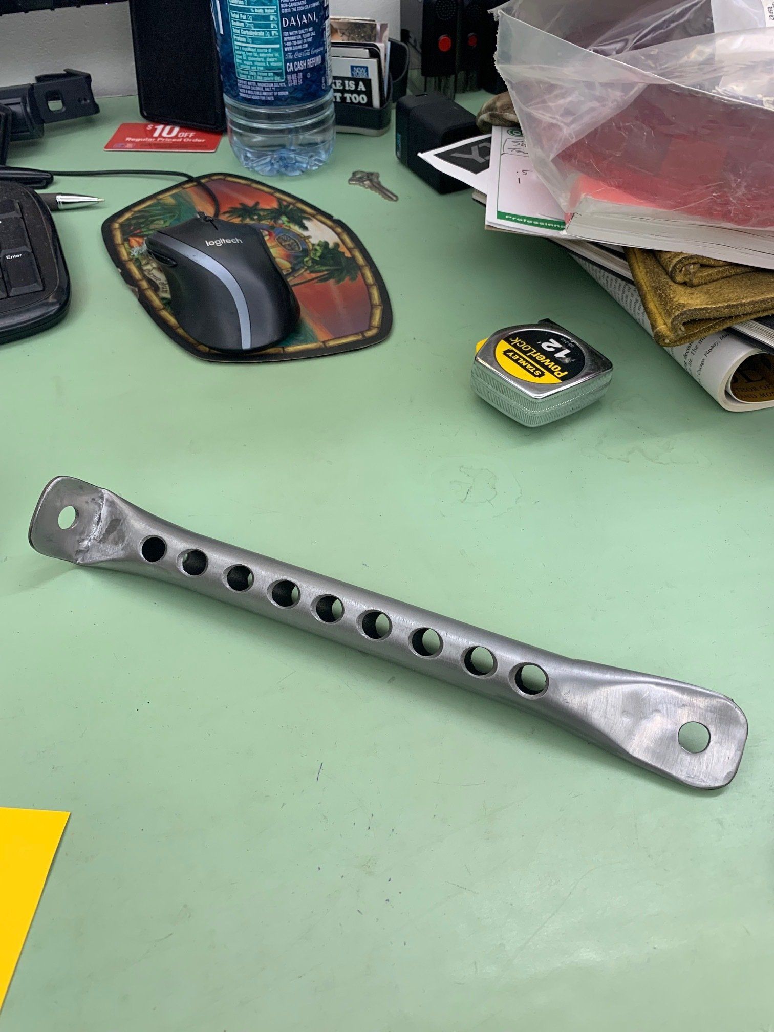 Metal perforated tool lying on a green desk beside a mouse, tape measure, and water bottle.