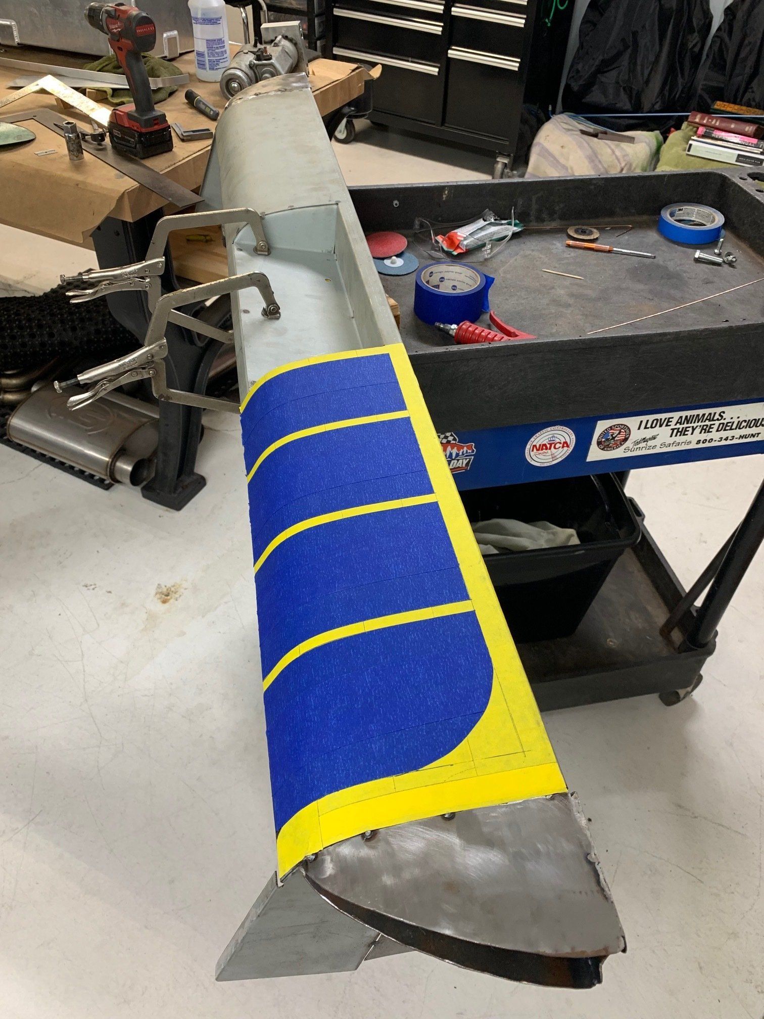 Blue and yellow striped model aircraft wing on a workbench in a workshop