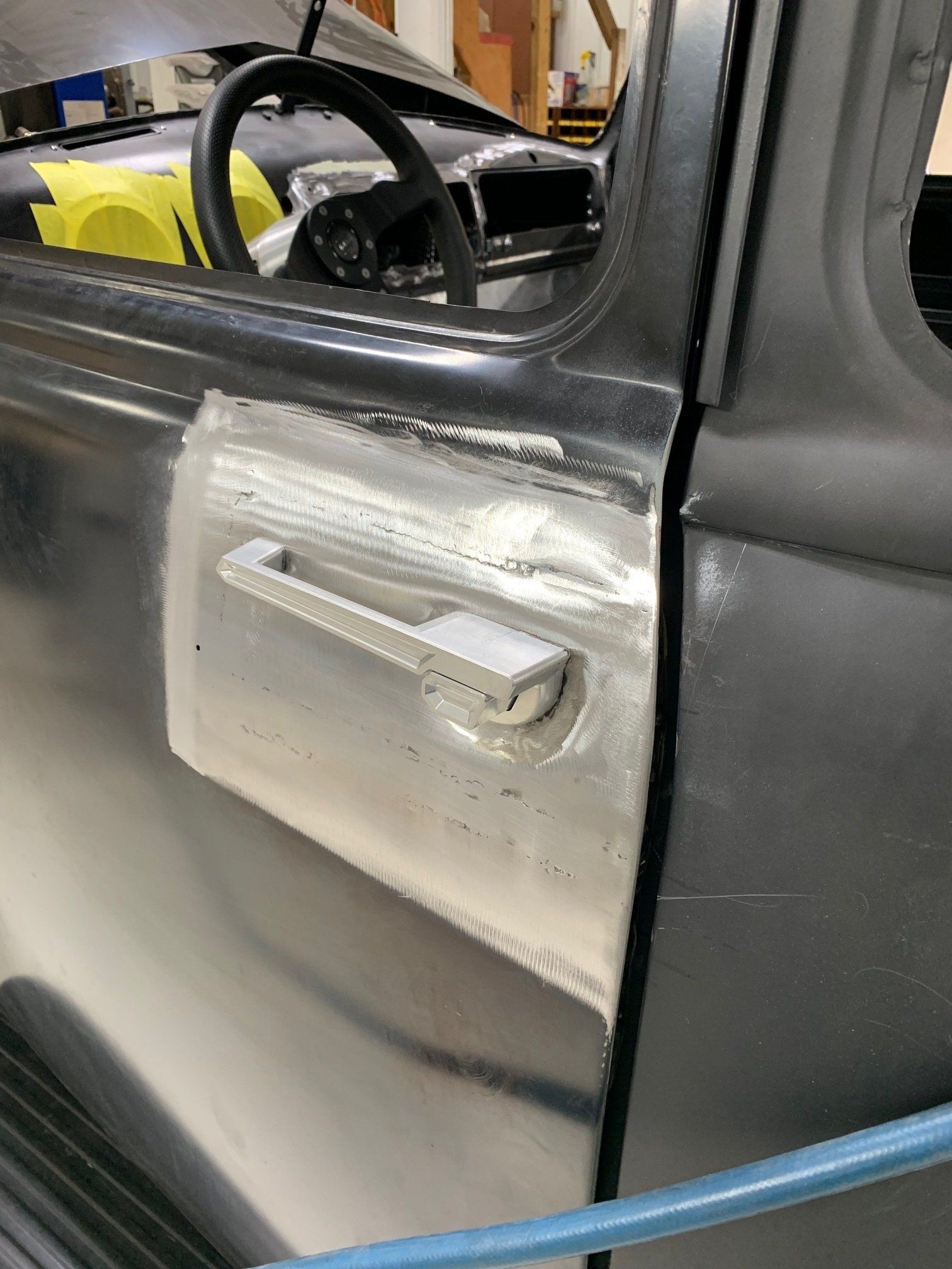 Close-up of a black car door with a silver panel and handle, partially open in a garage.