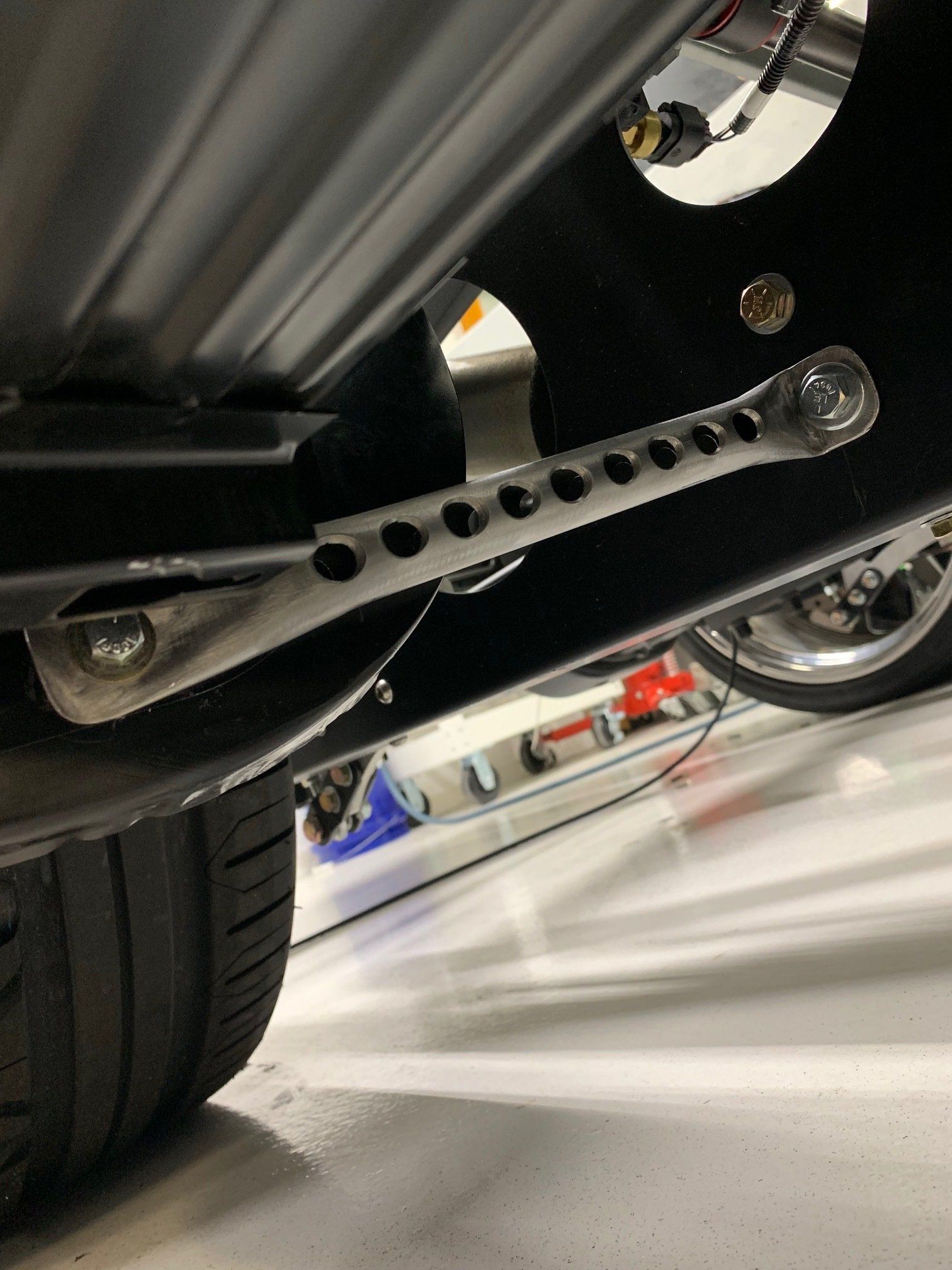 Close-up of a car’s undercarriage, showing a silver perforated suspension arm near the wheel.