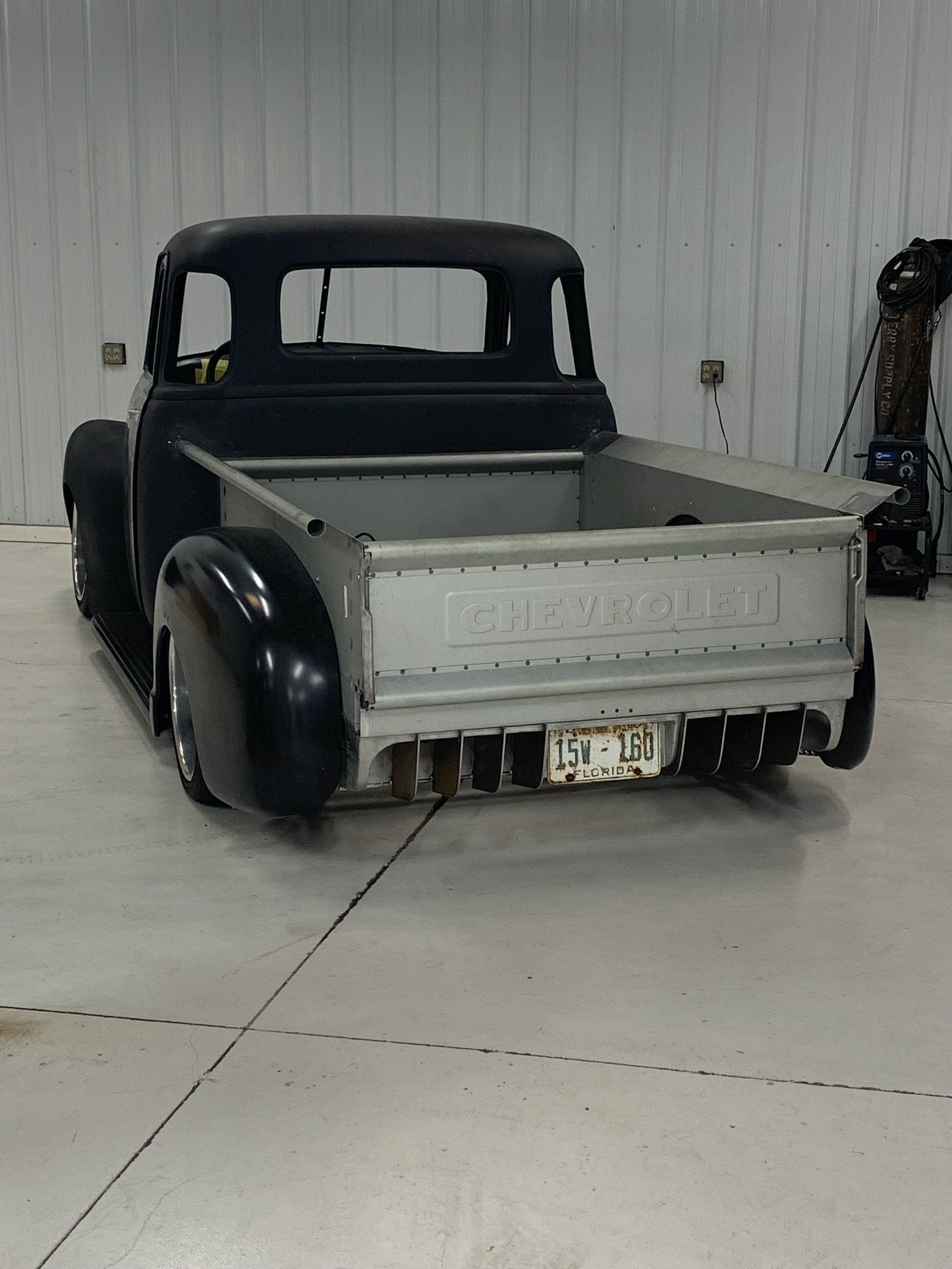 Vintage black pickup truck with a gray bed and fenders, parked in a garage-like space