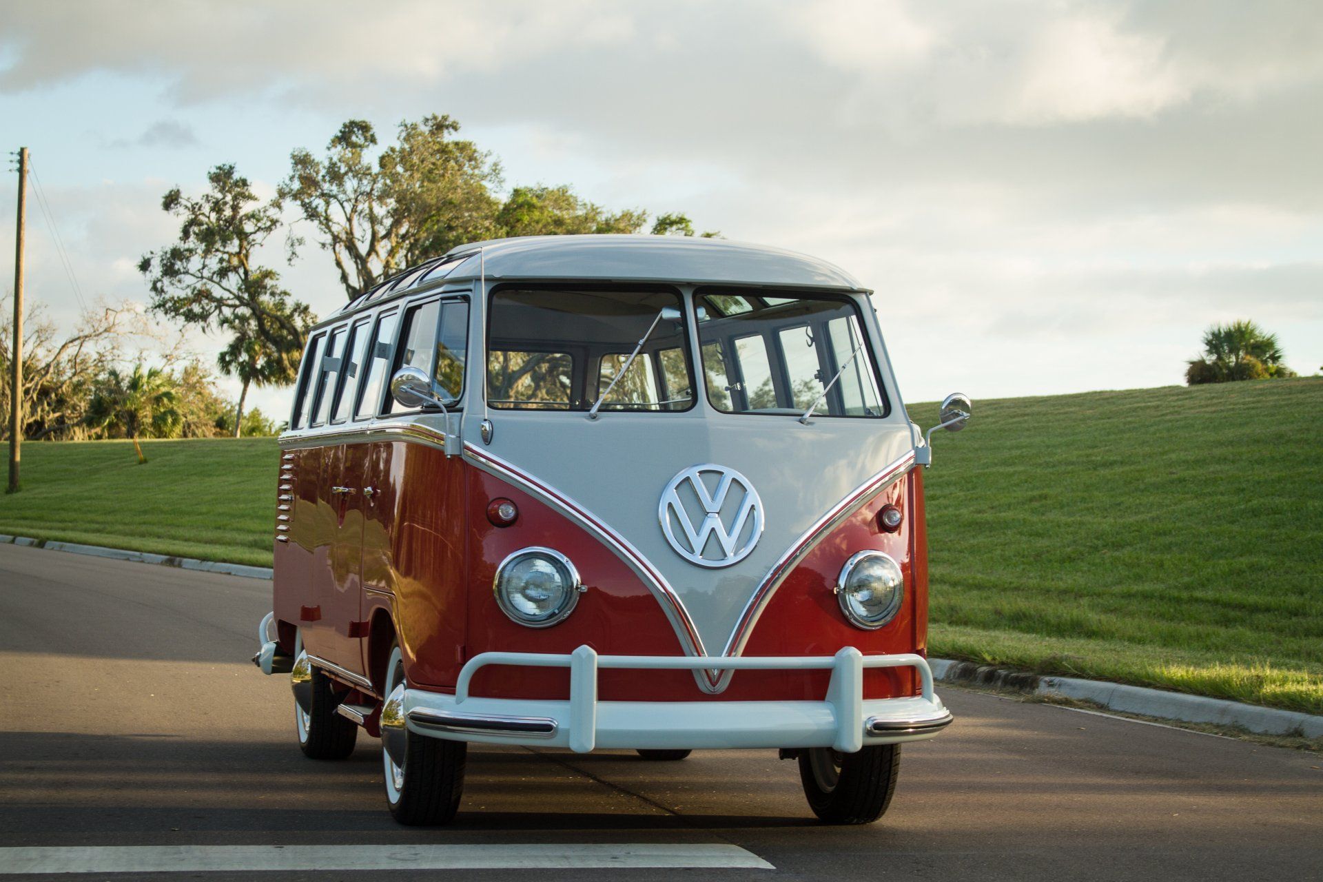 Red and white vintage Volkswagen van driving on a paved road beside grassy hills.