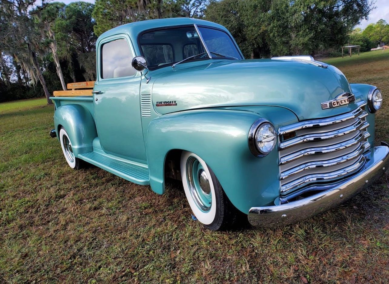 Vintage turquoise pickup truck with whitewall tires parked on grass, front three-quarter view
