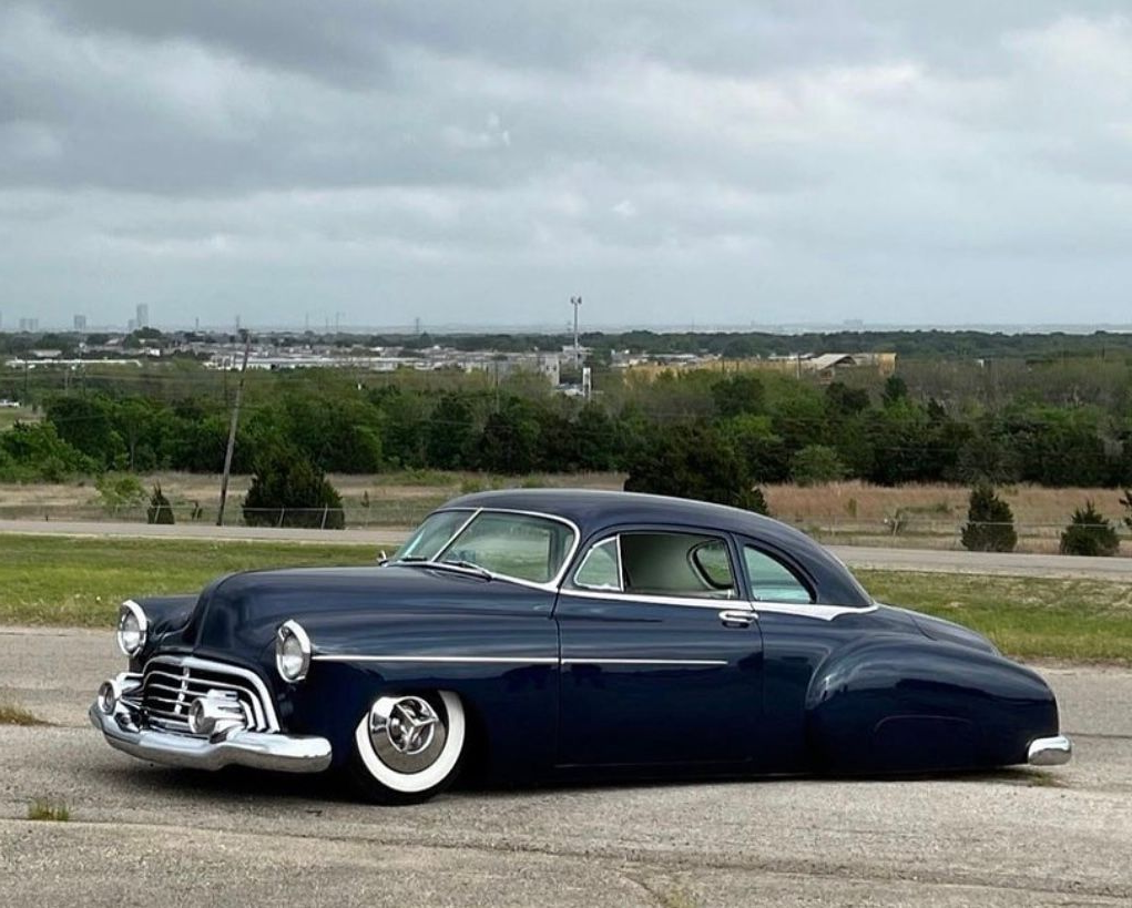 Dark blue vintage lowered car parked on a road with a city skyline in the distance