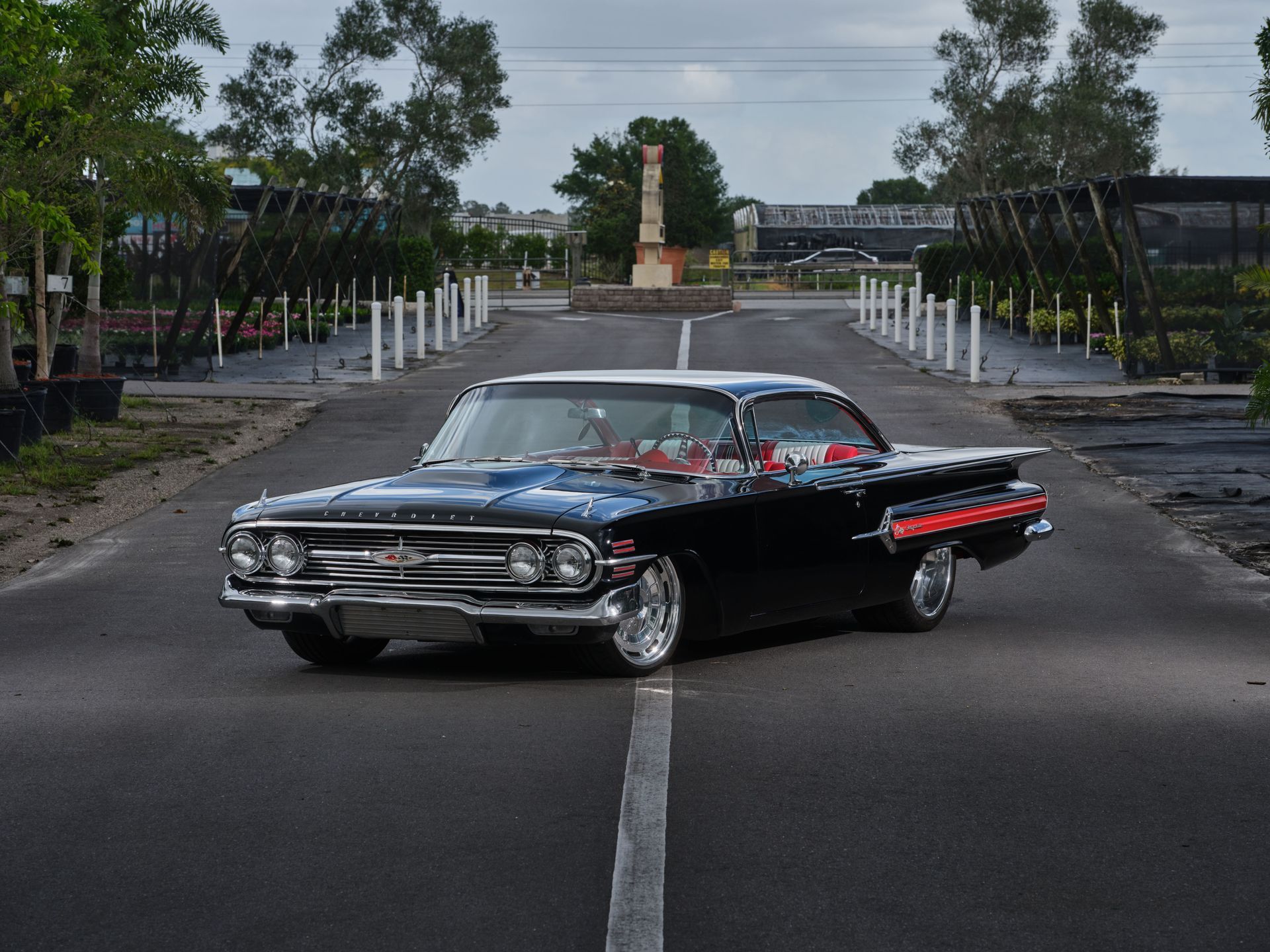 Black classic car parked on a road with trees and white posts in the background