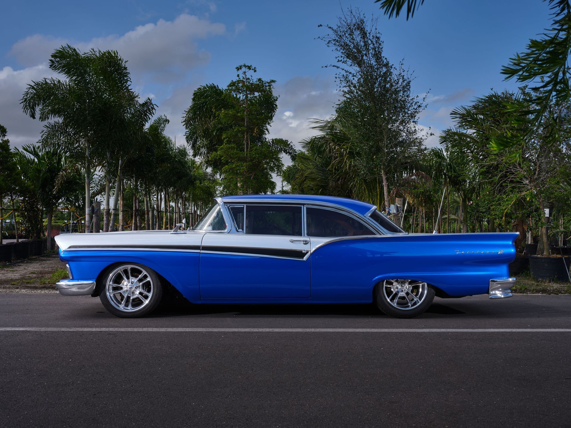 Blue-and-white classic car parked on a road with trees and blue sky in the background