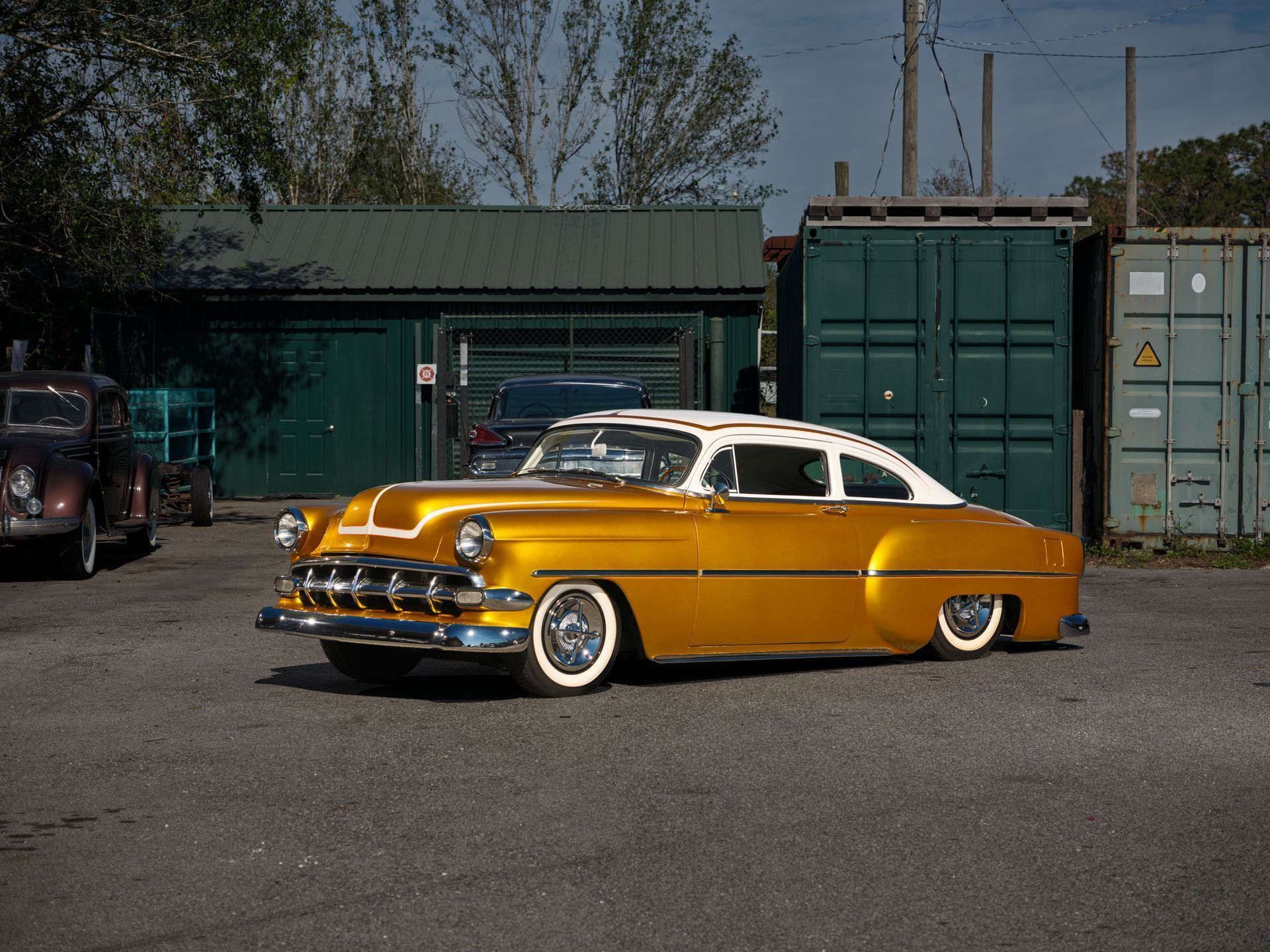Yellow vintage car parked in an industrial lot with shipping containers in the background