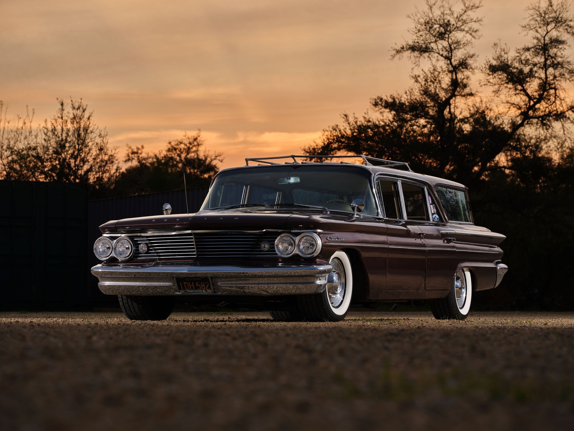 Classic dark station wagon parked on a road at sunset with silhouetted trees in the background