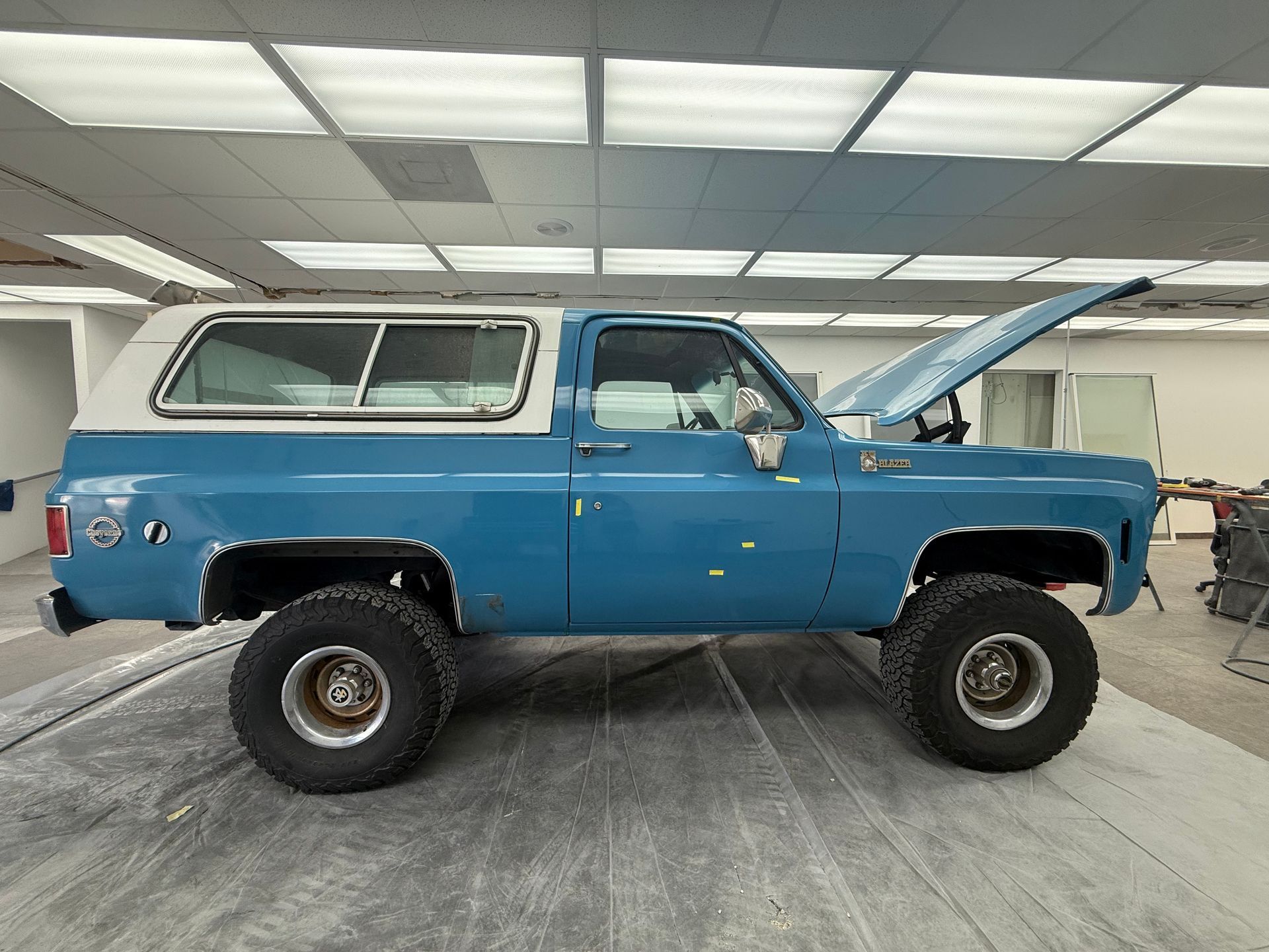 Blue lifted SUV with open hood in a garage, side view.
