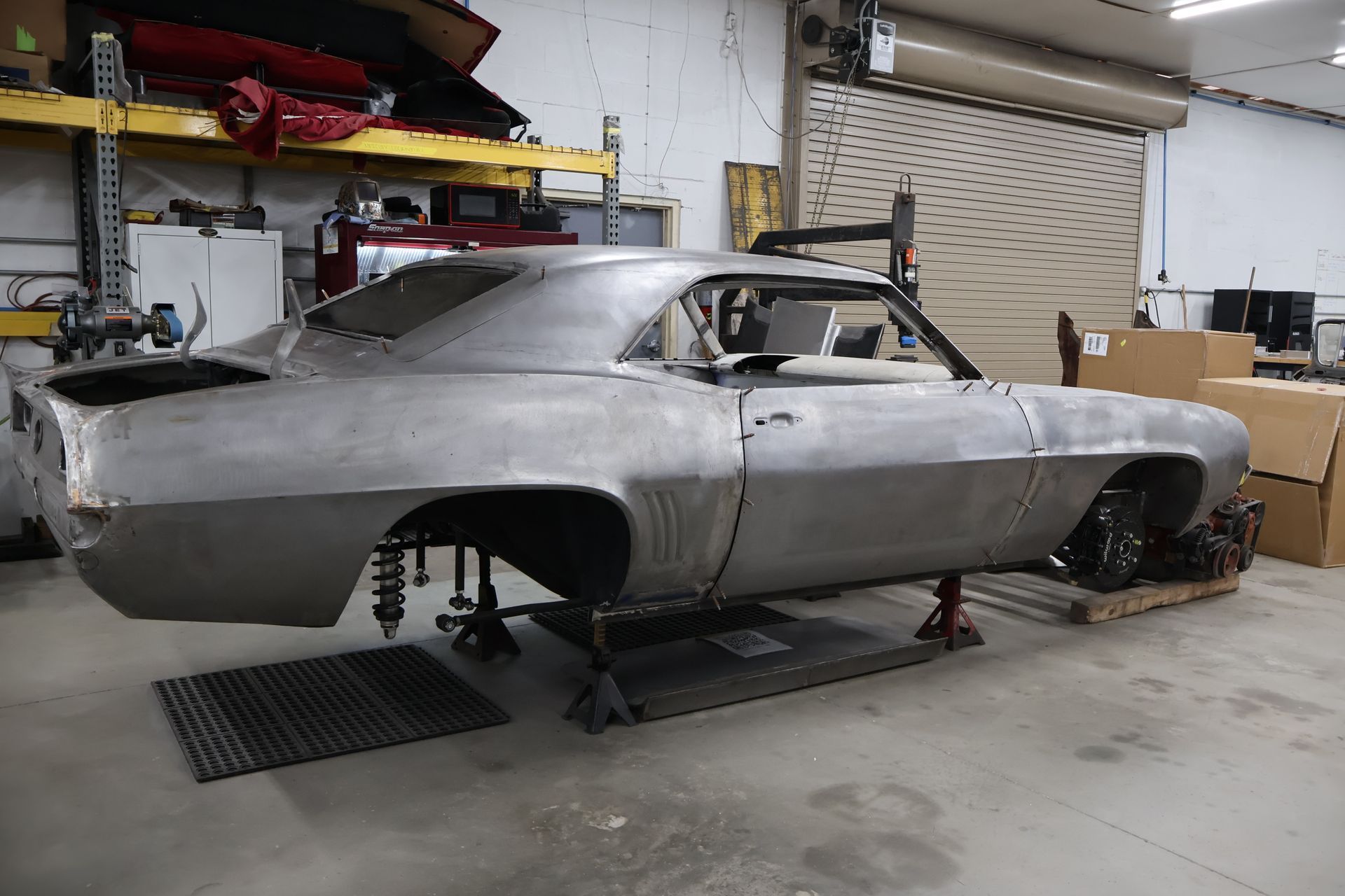 Partially restored classic car body in a garage, stripped to bare metal on jack stands.