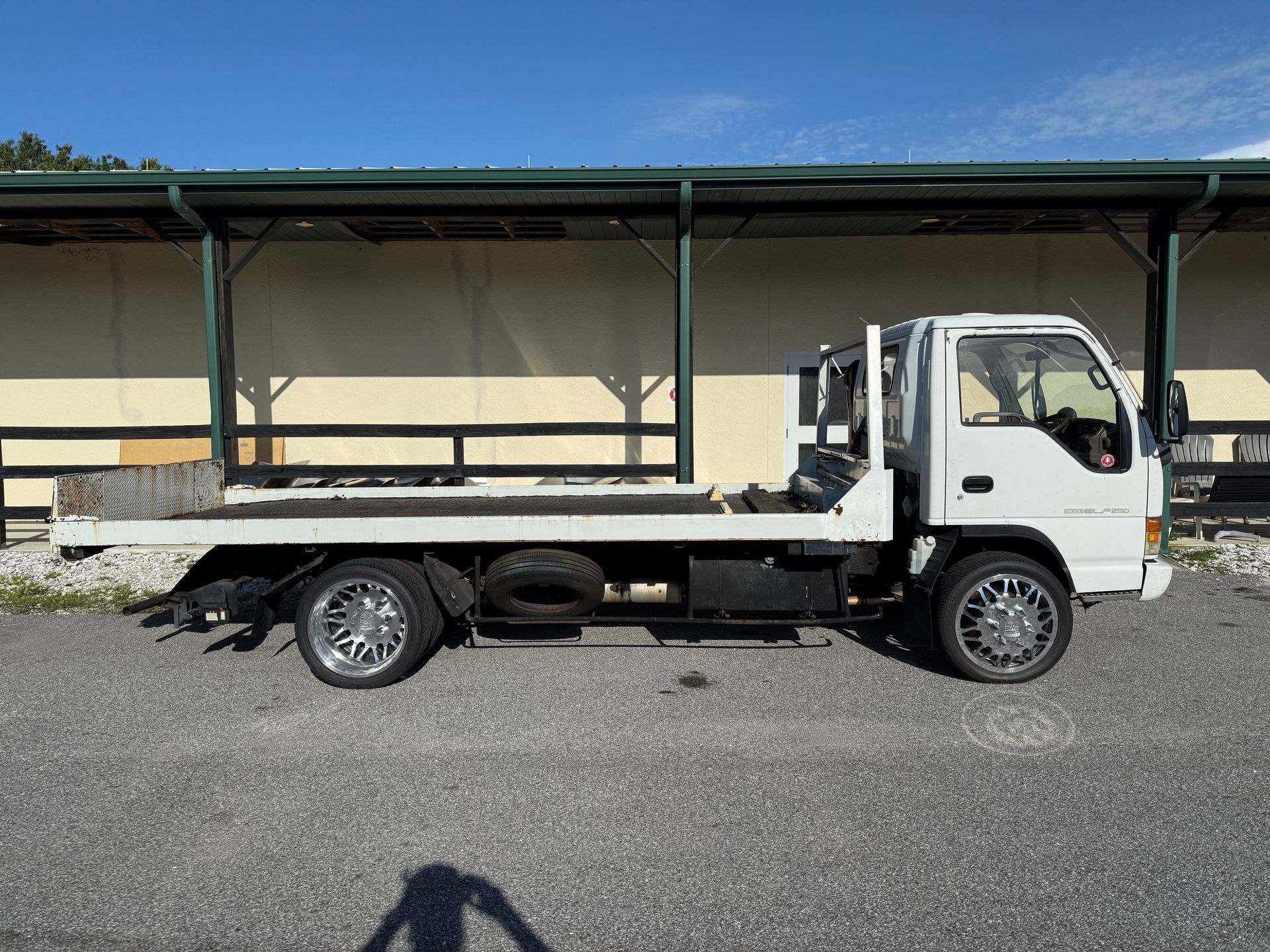 White flatbed truck parked on gravel beside a covered loading area