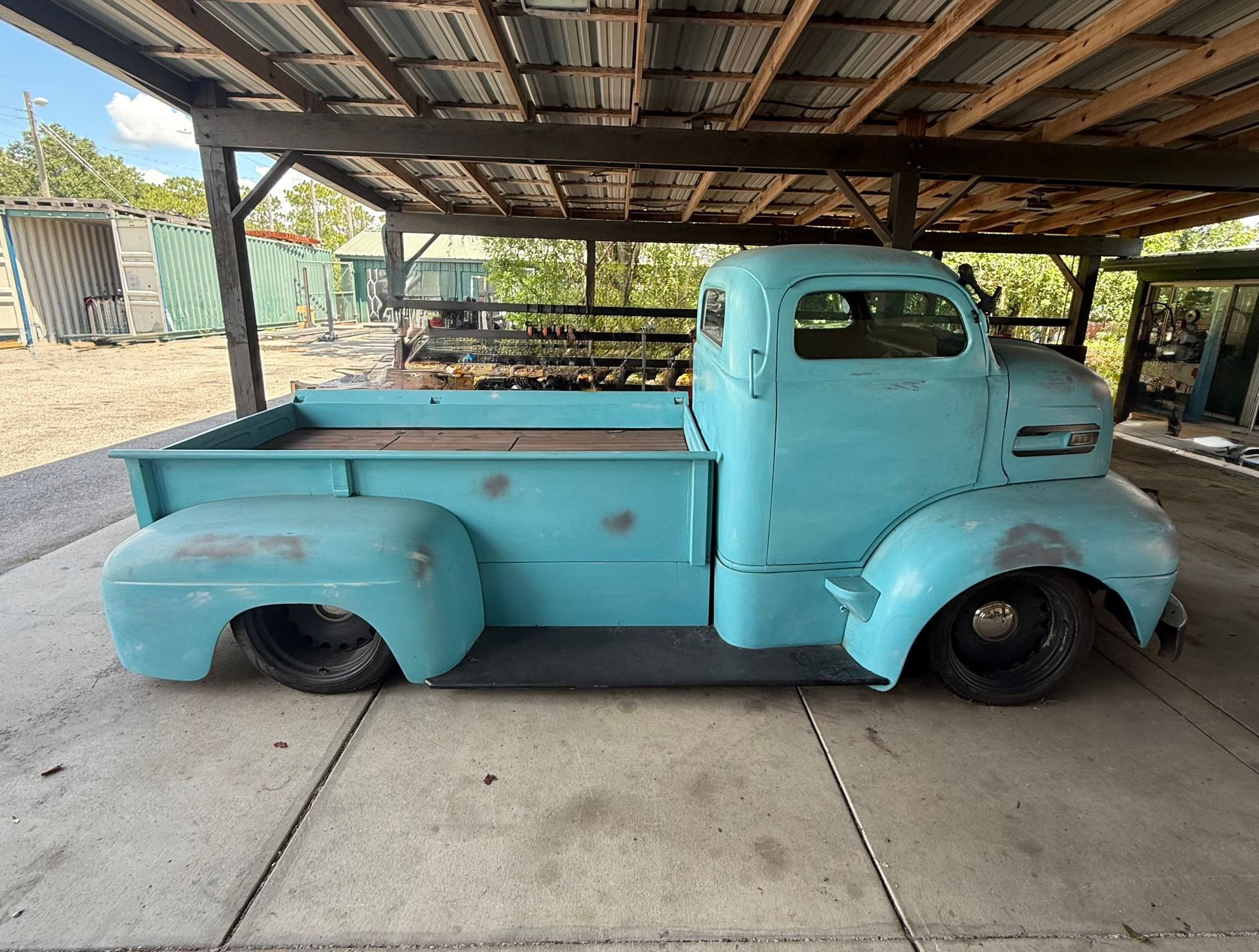 Turquoise vintage pickup truck parked under a metal carport